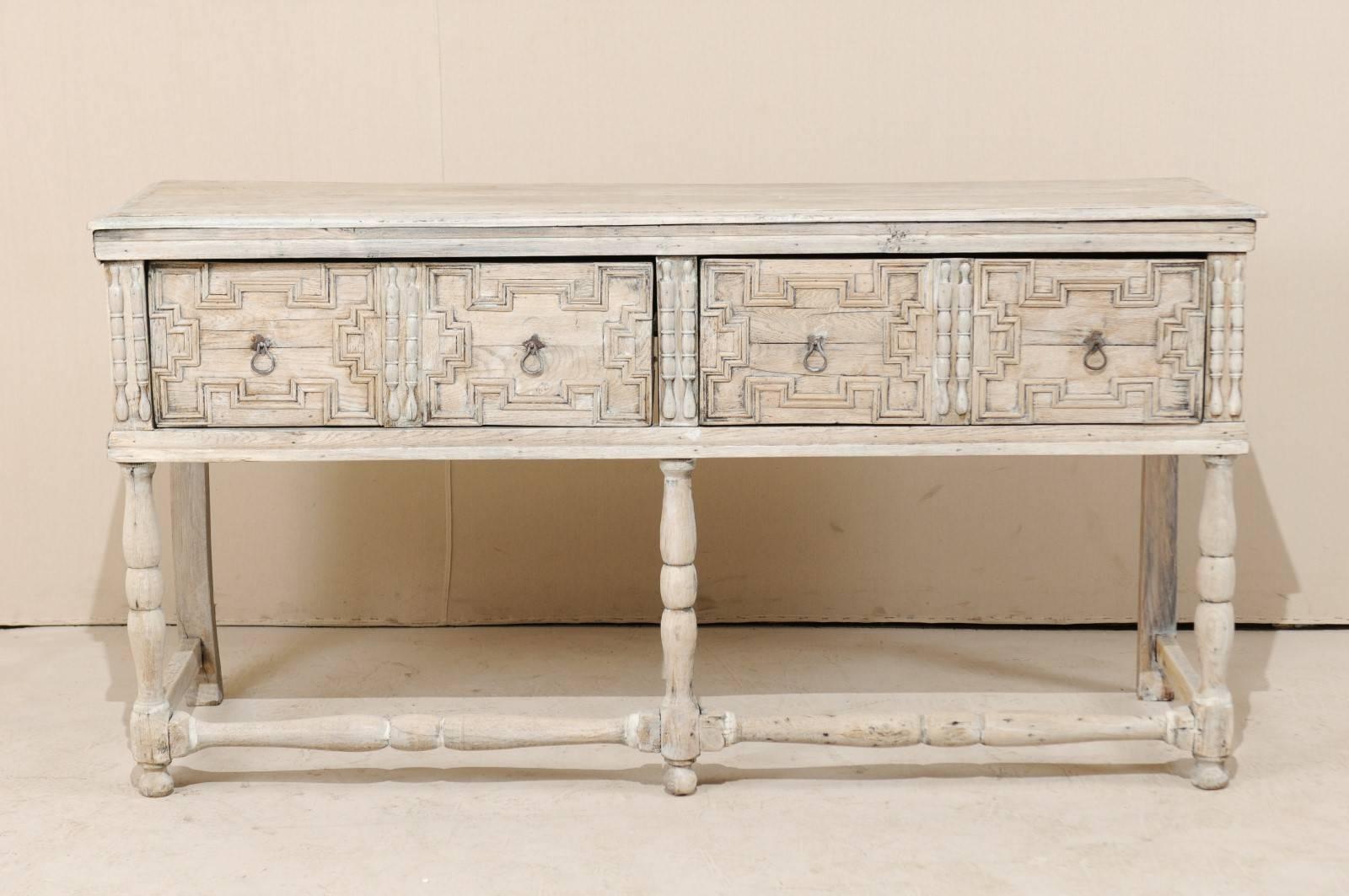 An 18th century English console table. This English console table, from the 18th century, features two large drawers which have deep, geometric carvings, carved vertical accents and original hardware. The table has turned legs and stretchers across