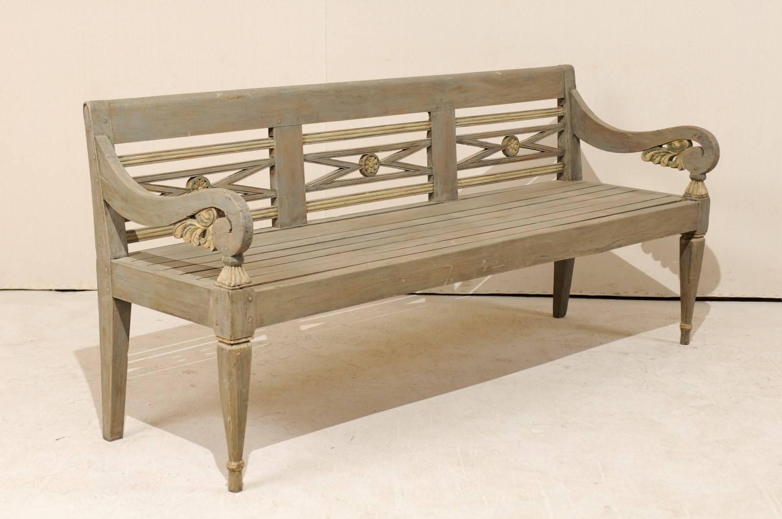 A painted teak wood sofa bench. This Dutch Colonial style painted teak bench is from the mid-20th century, Indonesian. The bench has swagged arms with a carved leaf motif and scroll at the knuckles, tapered front legs and a horizontally designed,