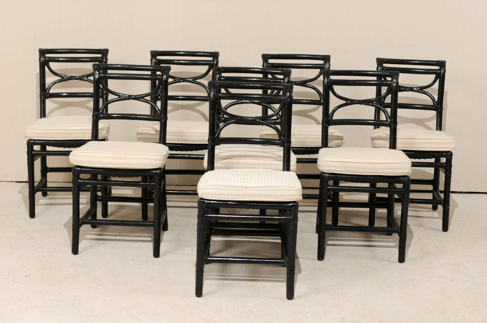 A set of eight vintage McGuire rattan side chairs. This set of side chairs from McGuire furniture maker, feature a rattan frame/body with a centered Curule back splat and outward curved top rail. The chairs are painted in a glossy black with
