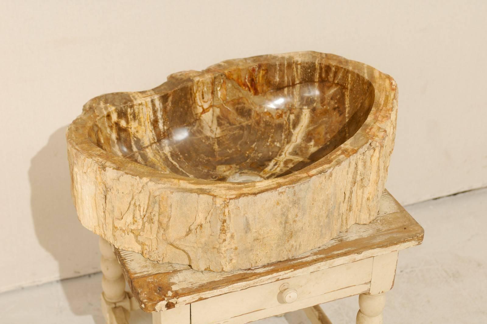 A petrified wood sink. This petrified wood sink has more of an oval shape with a flatter back-side. The colors are primarily in brown, beige and cream tones, with cream/beige being the prominent exterior surround color, and brown with lighter