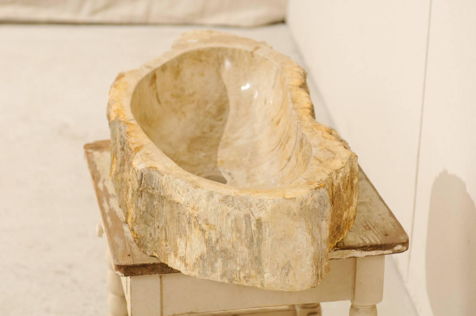 A cream and beige color petrified wood sink. This petrified wood sink features an oblong shape. The sink is primarily cream and beige with some warmer veining and spots throughout. The interior of the sink has been polished and the surround has been