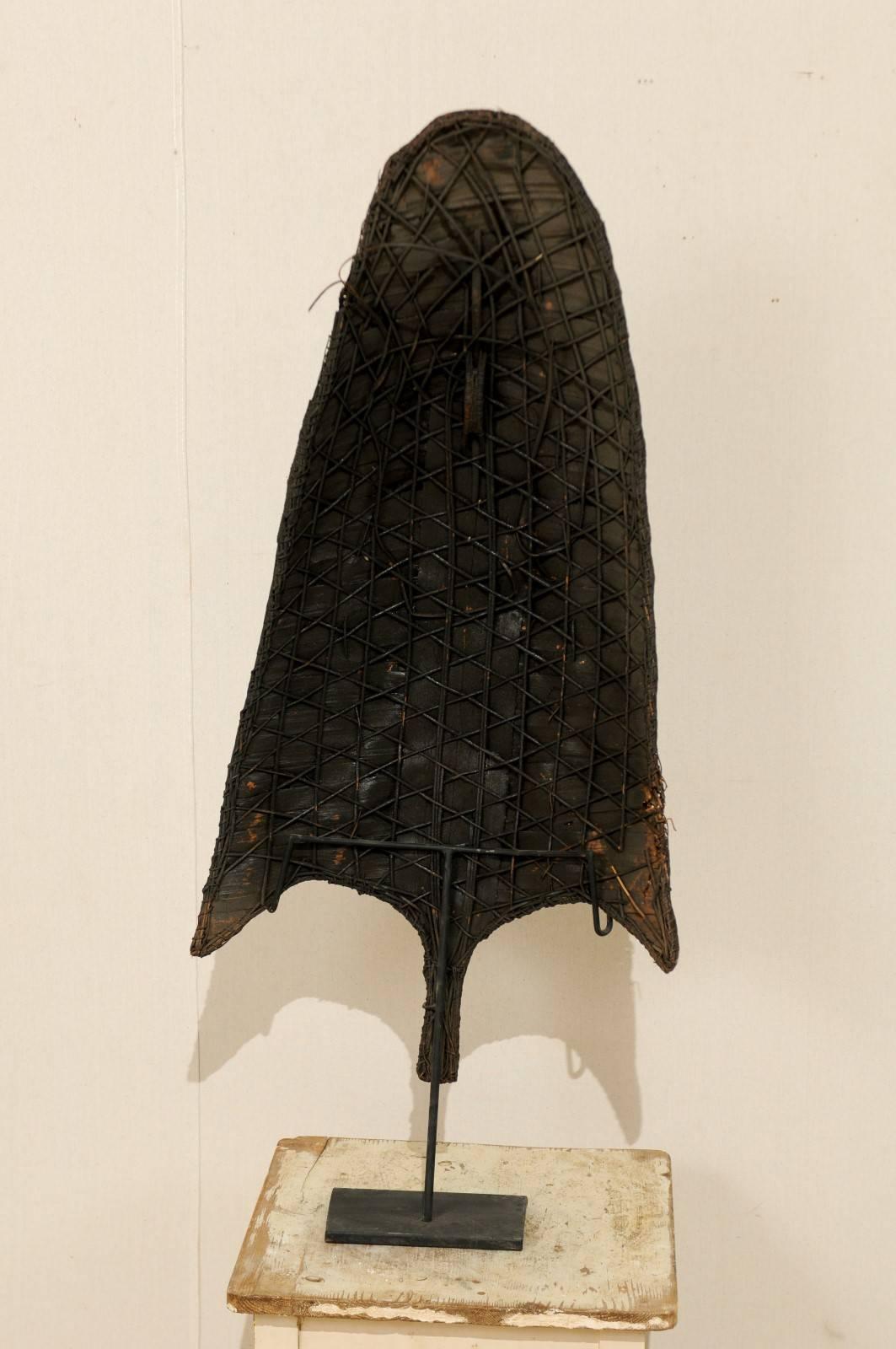A Naga rain shield on custom iron stand from the Northeastern part of India. This Naga rain shield from the mid-20th century is constructed from interwoven cane and fiber and is beautifully aged. The shield is held upright on a custom black iron