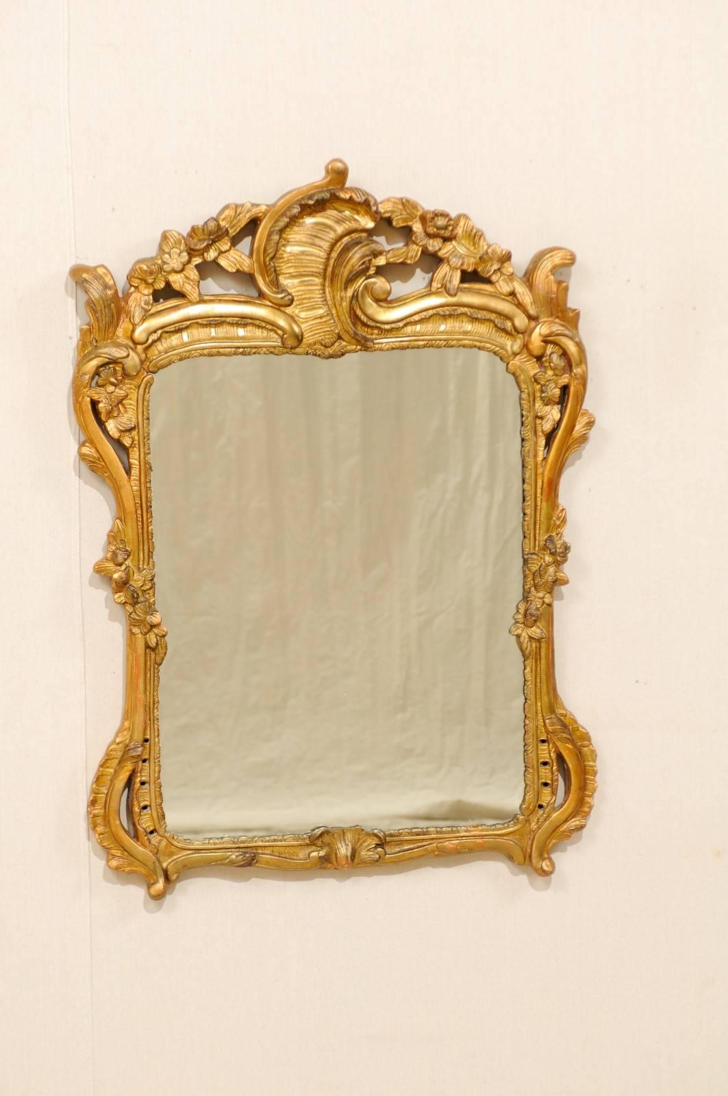 An Italian Rococo style wood carved mirror. This 19th century Italian rectangular shaped mirror features a richly carved raised crest in a floral and leaf motif. The sweetly carved flowers are repeated and hug the mirror at each center side. The