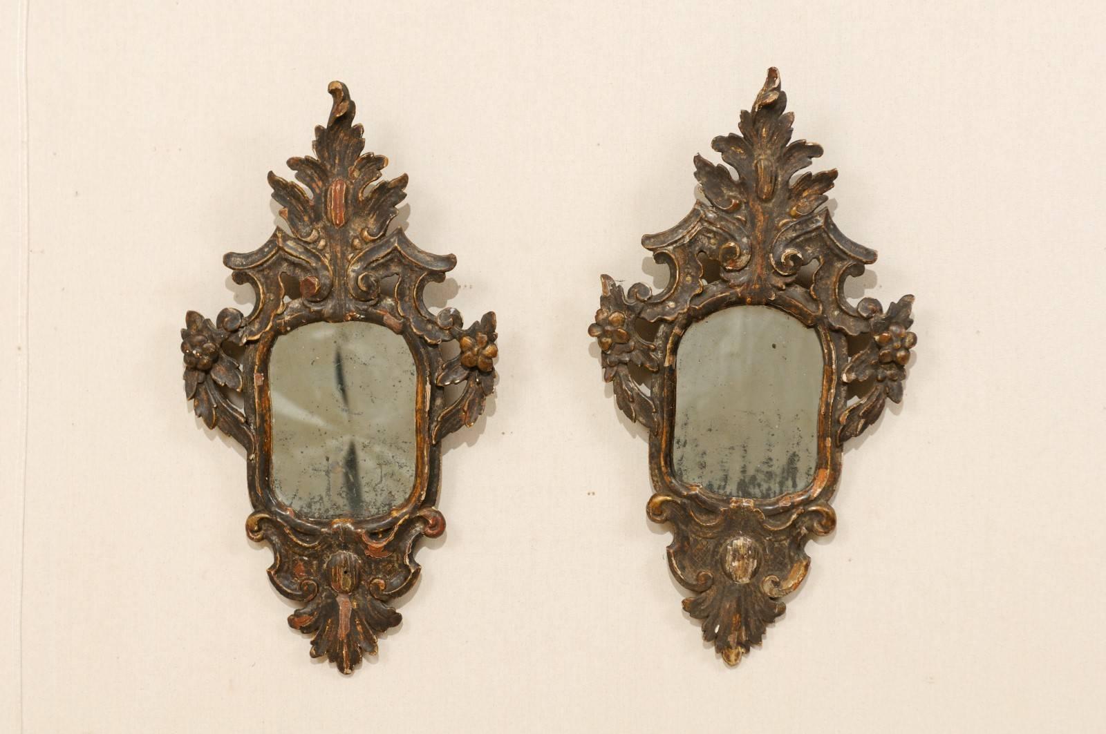 A pair of 18th century elegant Italian mirrors. This pair of Italian wooden Rococo style mirrors are beautifully carved in floral and leaf motifs. The crests and skirts are elongated and rich in detail. The mirrors are gesso over wood and gilding,