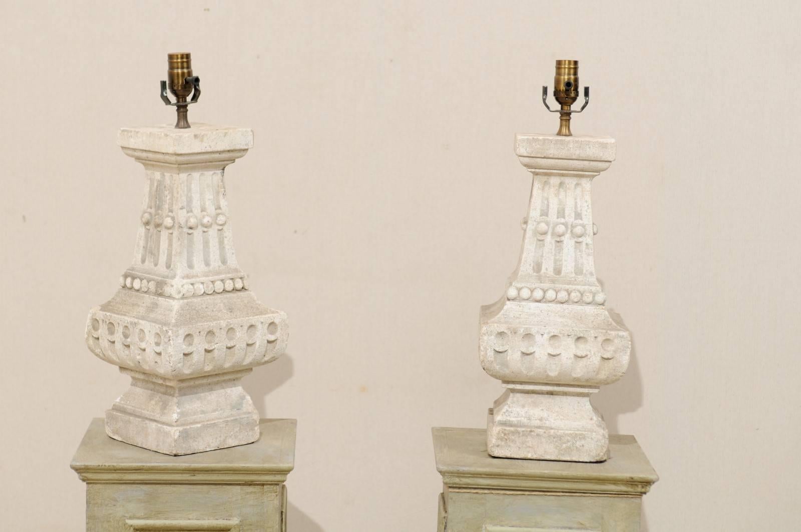A pair of French cast stone table lamps. These pair of French table lamps from the mid to late 20th century has an elegant cast stone baluster form, and beautifully-weathered surface. The lamps are adorned with a series of convex and concave