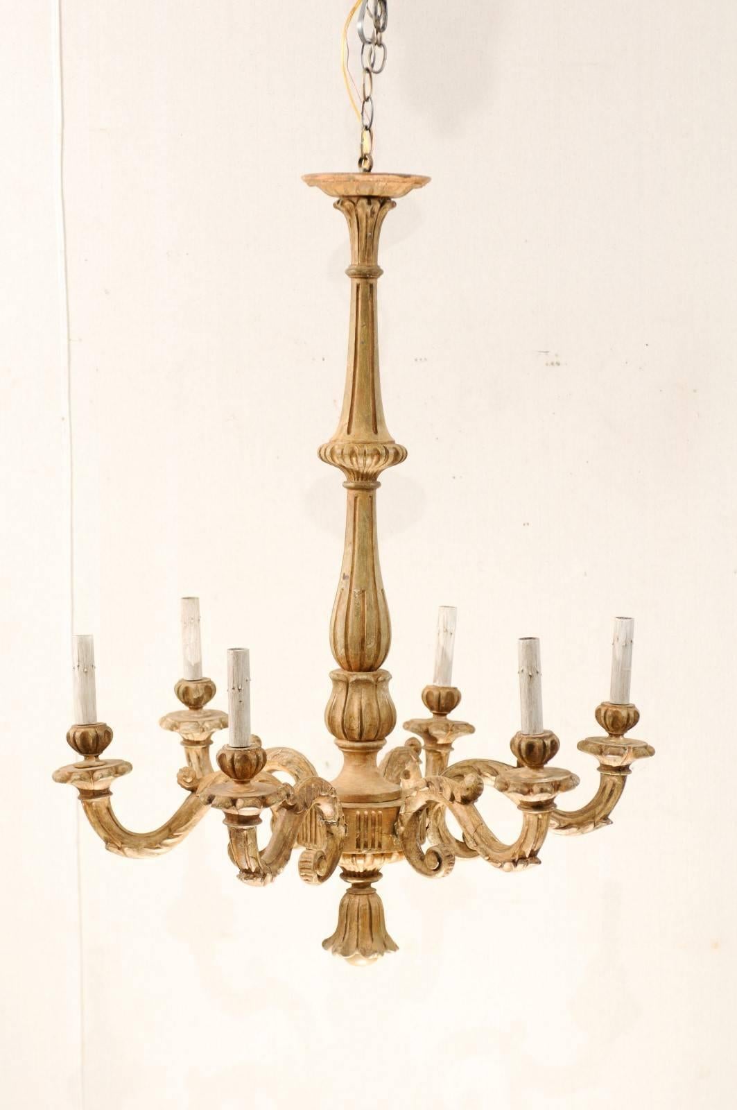 An Italian early 20th century six-light nicely carved wooden chandelier. This tall Italian chandelier features a long and slender central column. Six s-scrolled arms flow from the bottom of the central column, leading outwards towards its candle