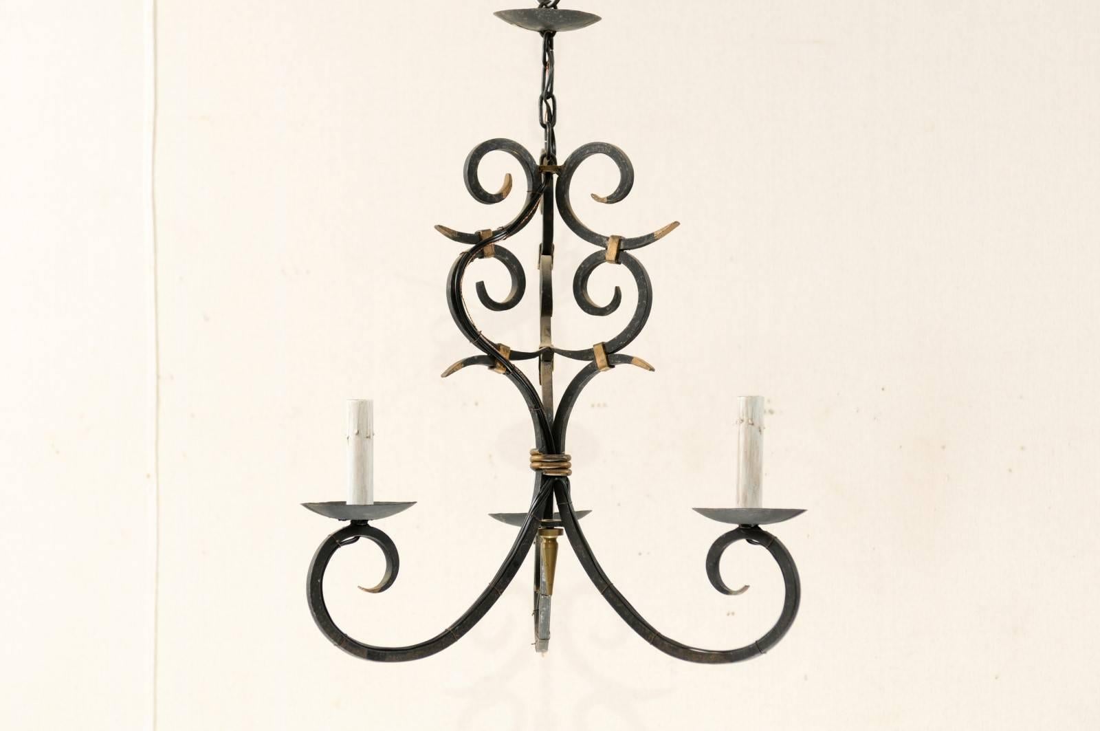 A French forged iron three-light chandelier. This dark colored French mid-20th century chandelier of forged iron is made of scrolled arms and scrolled crest with gilded elements. This French chandelier has also been rewired for the US and comes with
