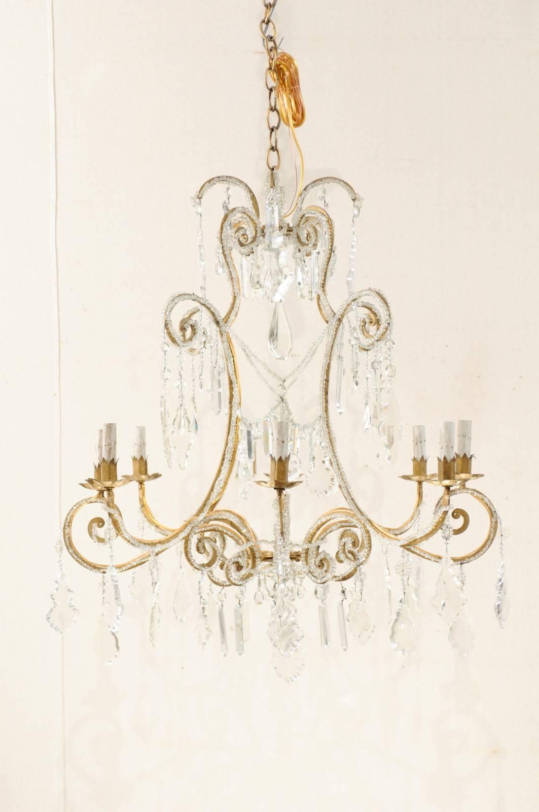 An vintage Italian crystal eight-light chandelier with scroll arms. This Mid-Century Italian gilded iron chandelier, with it's open and airy feel, is adorn with a collection of various crystals and various 