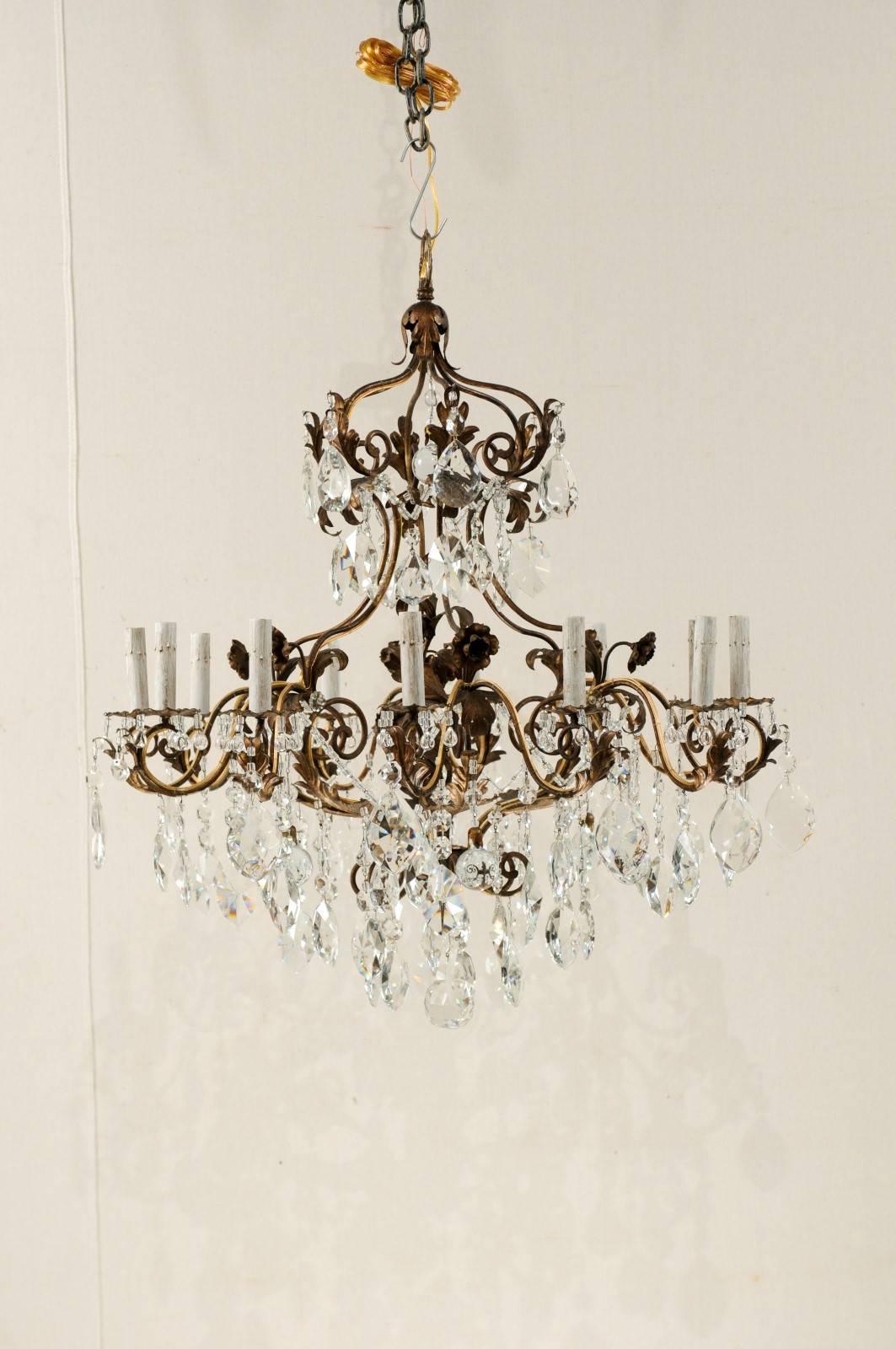 An Italian twelve-light crystal and iron chandelier from the mid-20th century. This elegant Mid-Century Italian twelve-light chandelier features and abundance of various faceted crystals with strung Italian glass beads stemming from the ornately