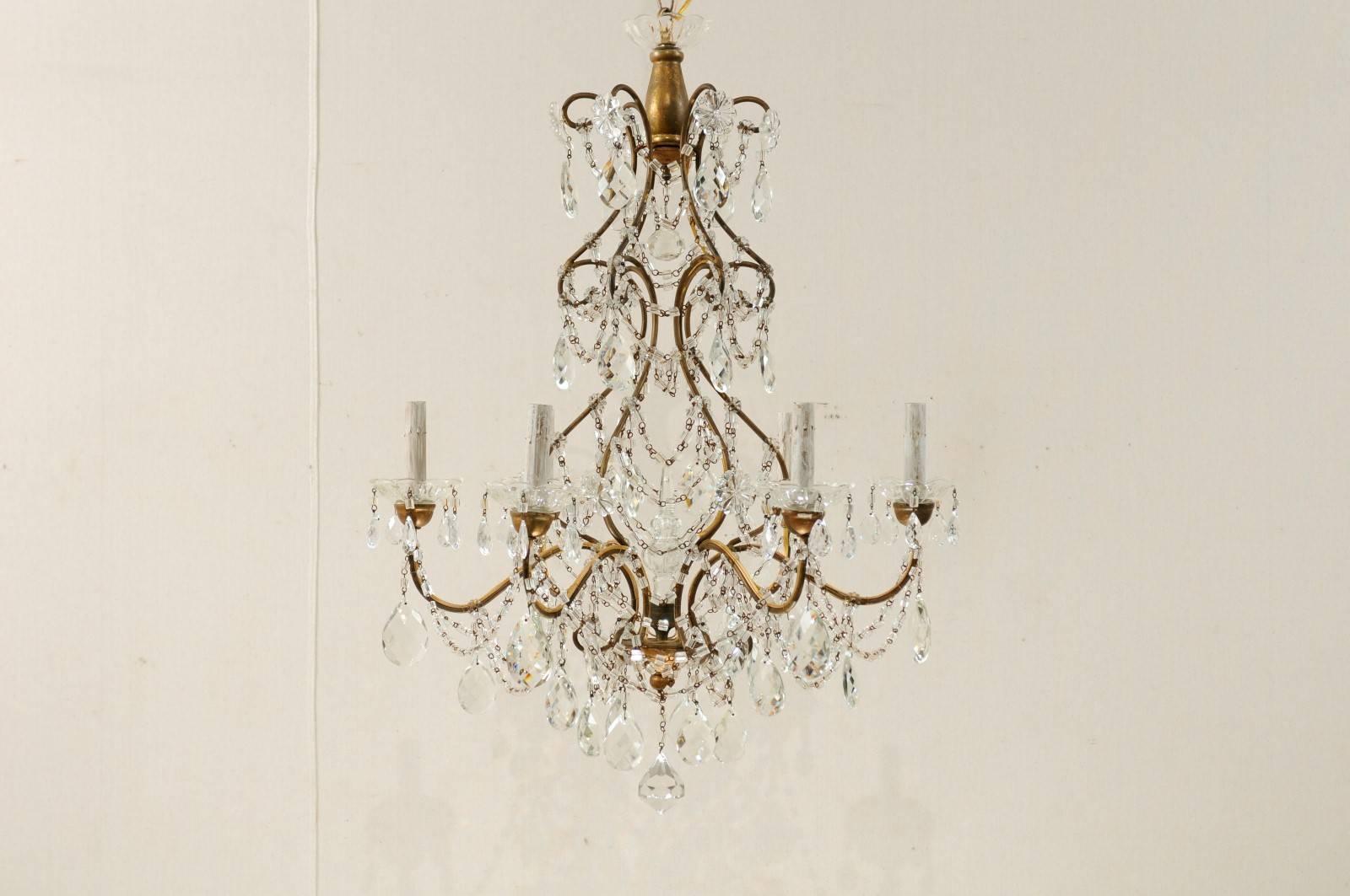 A pair of Italian crystal six-light chandeliers. This Mid-Century pair of Italian chandelier features a scrolled armature adorned with various crystals, strung with Italian glass beads. There is an large vertical crystal within the centre of the