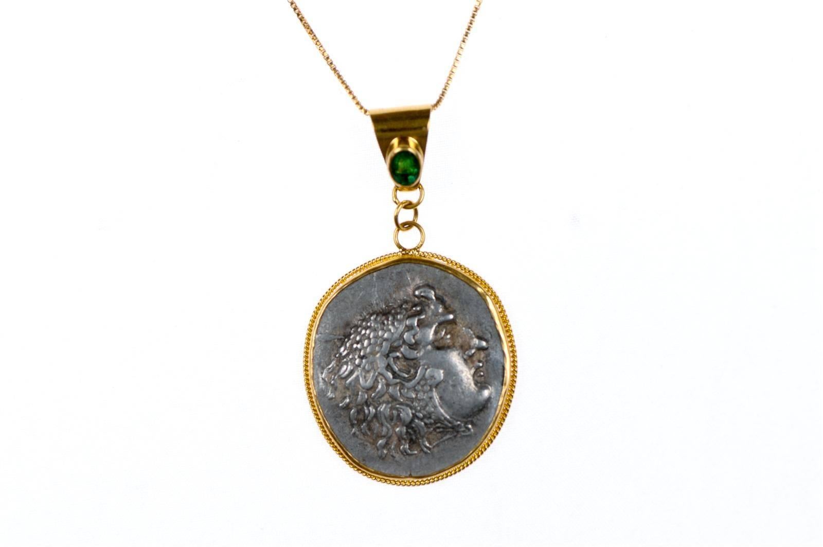 An Authentic Greek (Macedonian) Alexander the Great Tetradrachm Coin, 336-323 BC, set in a 22-karat gold bezel and Bail with an Emerald Stone Accent. Obverse of Coin is Heracles and Zeus Reverse. Coin pendant measures approximately 2 1/3