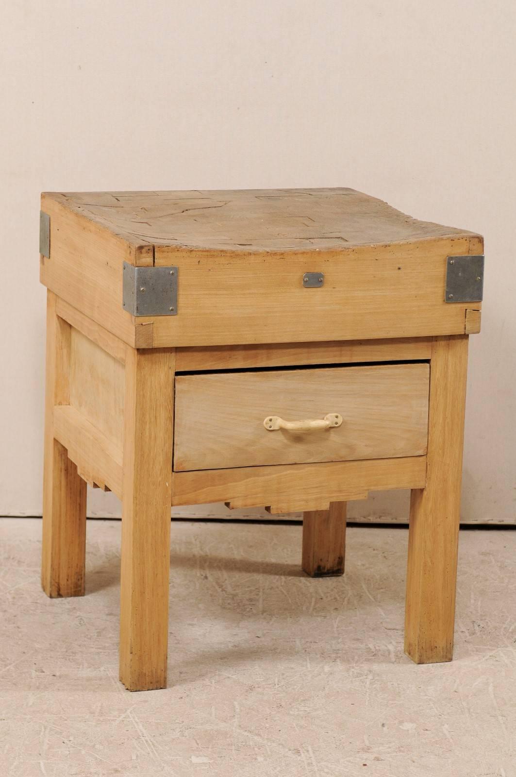 A vintage Swedish butcher block table. This square shaped butcher block table features a thick butcher block top over a single, large drawer. The top has wrapped metal plates at all four corners. The skirt has a graduated, step down feature carved