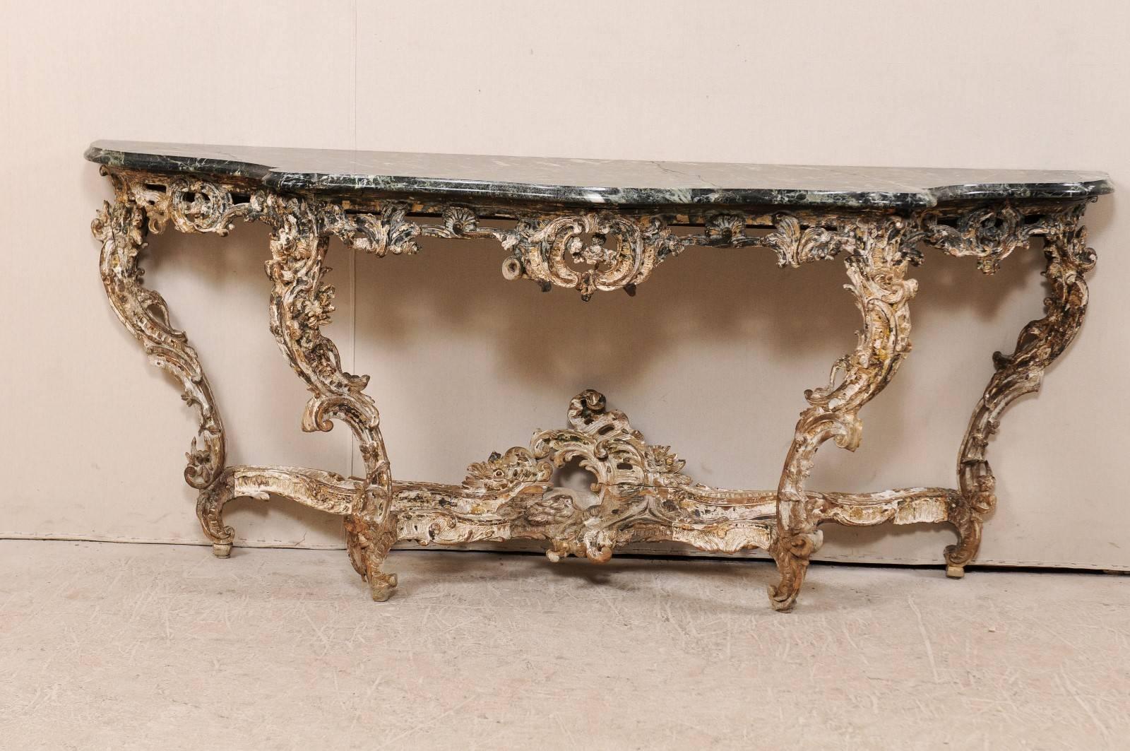 A French 18th century carved wood Rococo console table with marble top. This gorgeous French console table features the typical French elaborate carvings of the Rococo period along the skirt, cross stretcher and four legs. The base is gesso and over