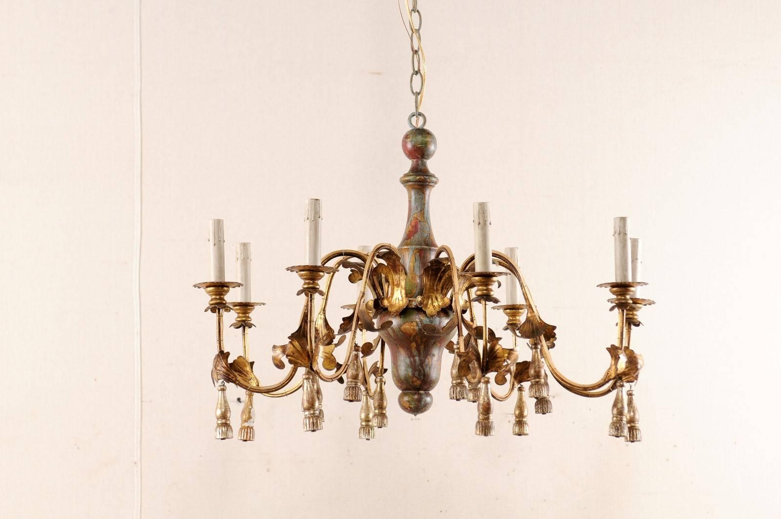 An Italian Mid-Century eight-light chandelier. This Italian vintage chandelier features a carved wood center with eight swooping arms decorated with tassels hanging from their lowest swoop, emerging from floral motifs. The carved wood center column