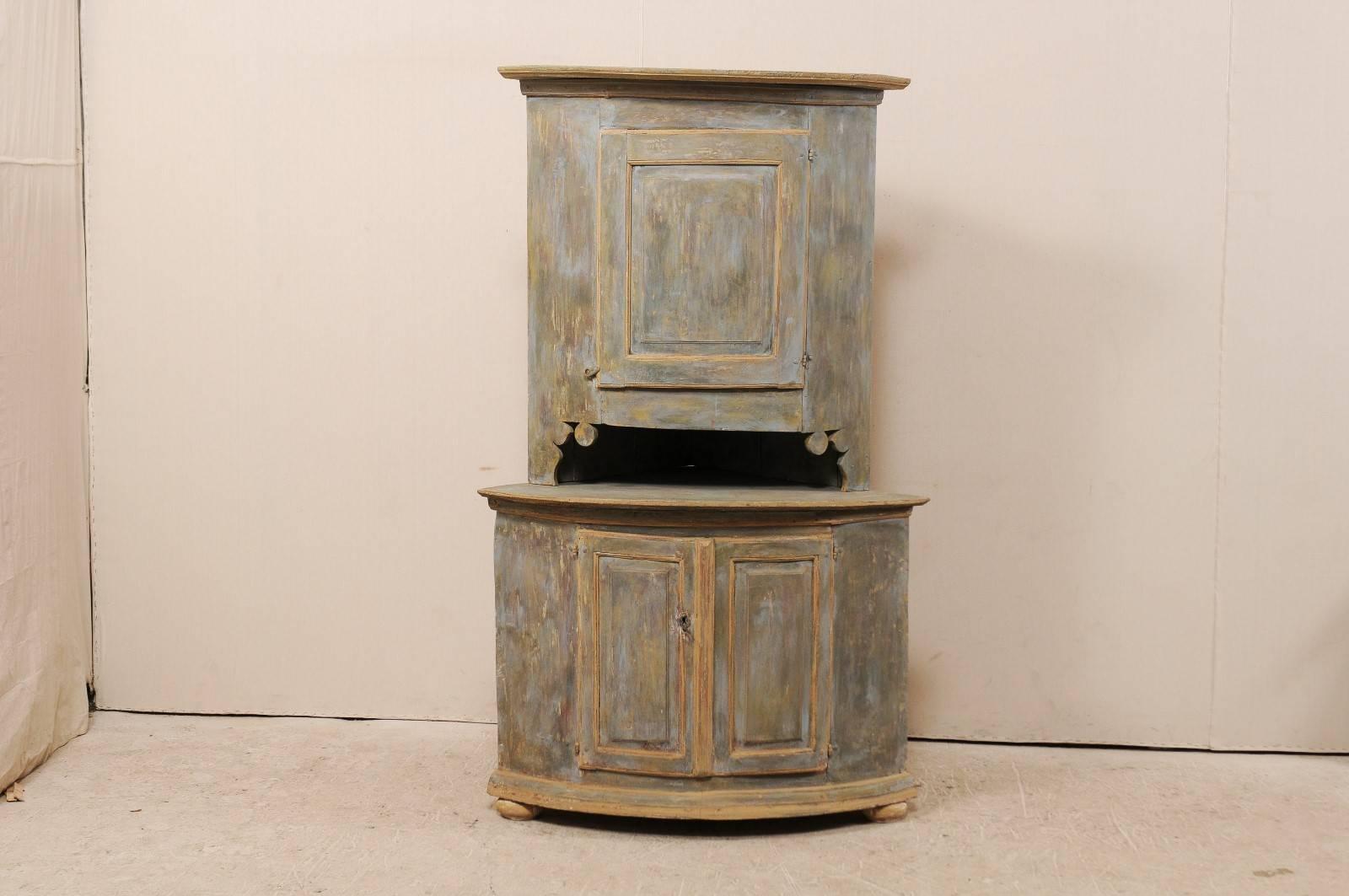 A 19th century Swedish painted wood corner cabinet. This Swedish cabinet, circa 1830-1840, features a single upper door over two lower, with an open section between the two pieces that can be used as a counter height shelf or work space. Both upper
