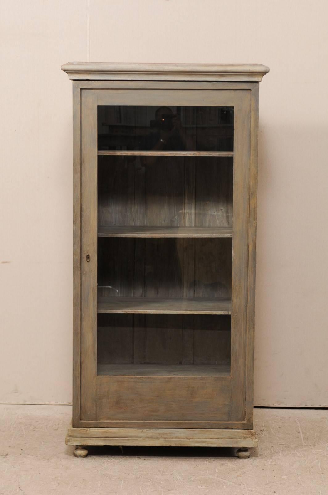 An early 20th century European painted wood vitrine. This painted wood display cabinet with single glass door features clean lines, accented by trim molding at the top and bottom, all raised nicely upon ball feet. The interior shelves are adjustable
