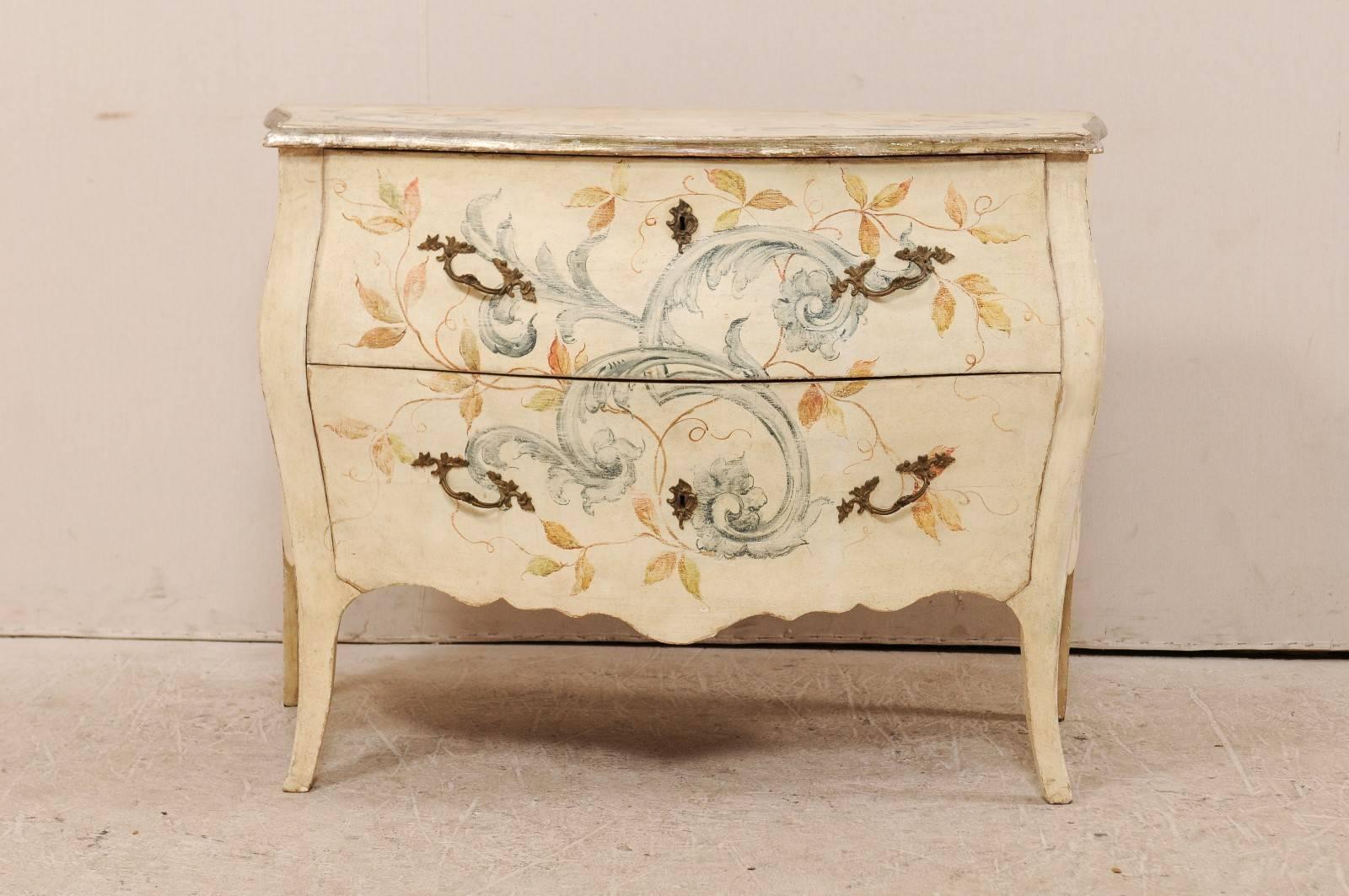 An early 20th century Italian two-drawer painted wood bombé chest. This Italian chest is ornately decorated in scrolling acanthus leaves and other foliage about the top, front and sides. The commode features two large sized drawers, with Rococo