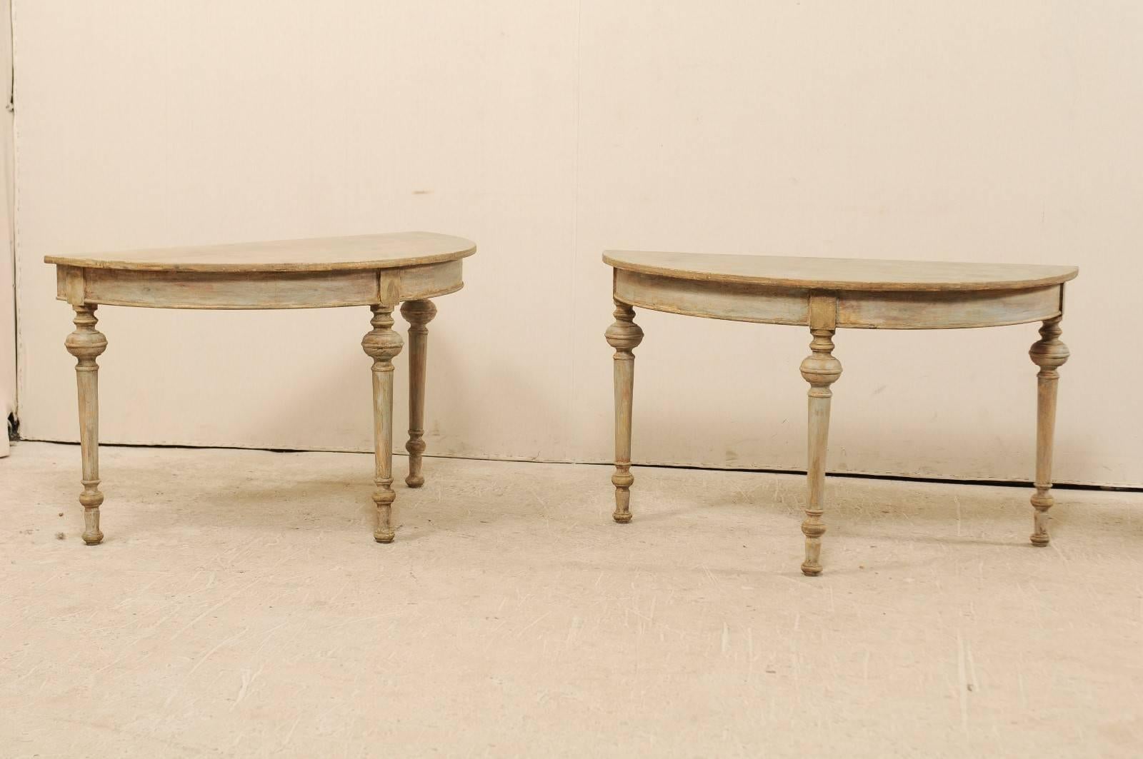 A pair of 19th century Swedish demilune tables. This pair of painted wood demilune tables features half moon tops over round aprons, raised on turned and slightly tapered legs. The overall color of these tables is a blue-grey with traces of green