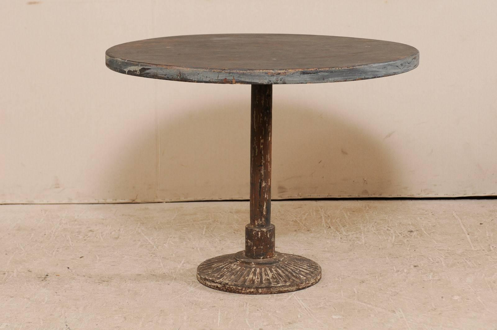A French bistro table. This vintage French table is round in shape and features a painted wood top and iron central pedestal base. The top is a dark, warm color with grey accent trim, and there is nicely aged patina throughout the top and base.