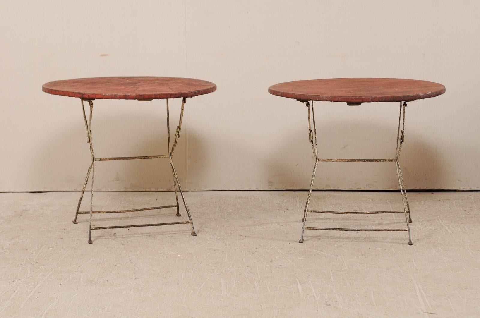 A pair of vintage French bistrot or café tables. This pair of round French tables feature folding tops that collapse and flatten the table for easy storage. These tables have their original red painted tops and white legs, with a lot of nice aged