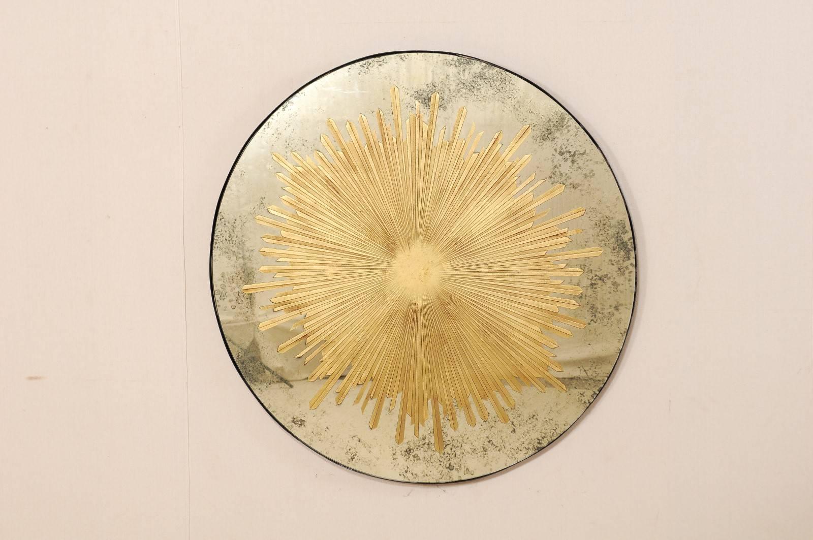 An American round-shaped mirror with starbust. This American custom artisan mirror features an exquisite gold sunburst encompassing much of it's center, atop an églomisé mirror. The starbust design is made of a series of alternating, thin rays