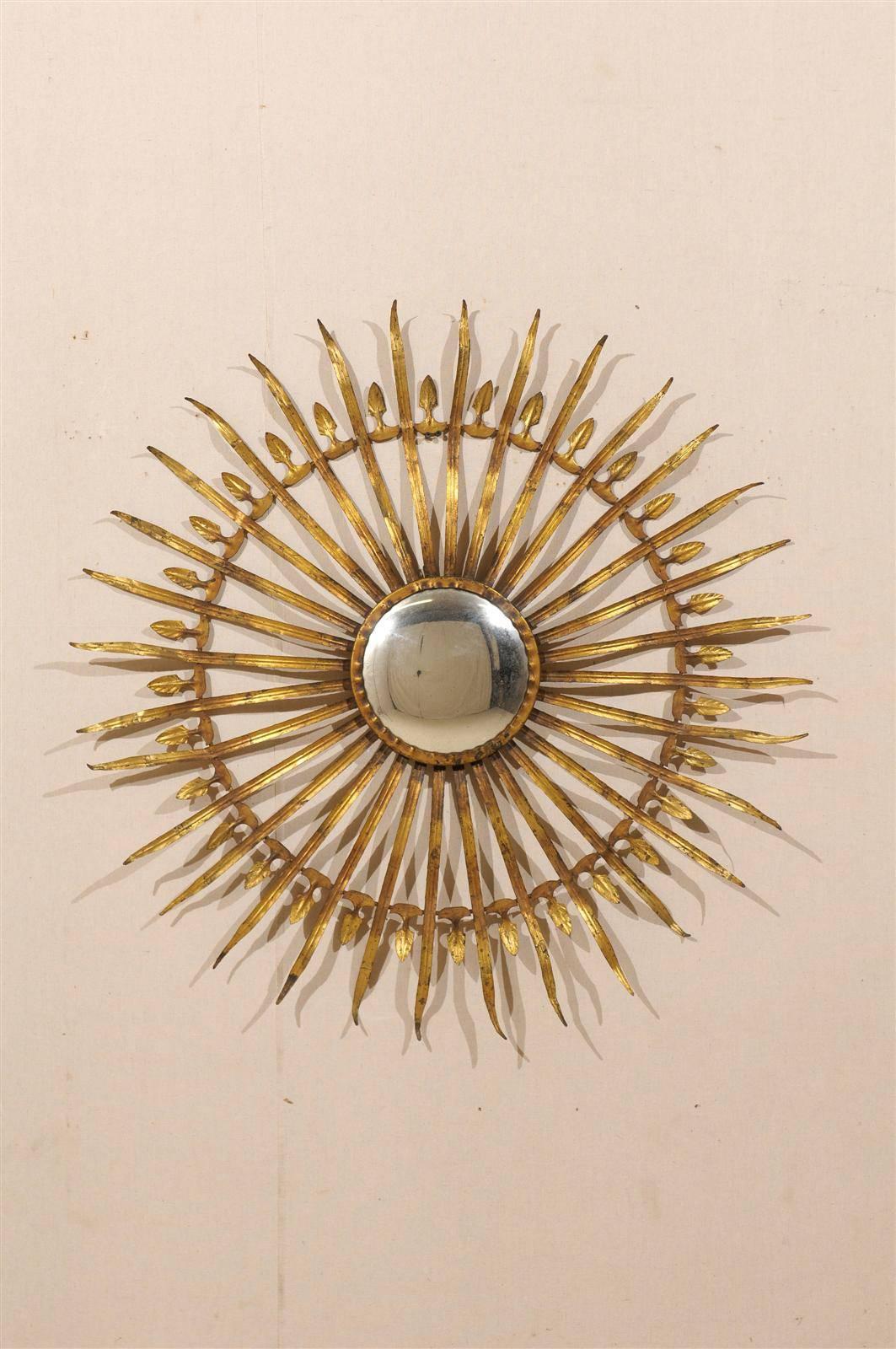 A French sunburst and foliage motif gilded metal wall ornament with round central mirror and nice patina. This French gilt metal mirror features a halo of undulating leaves radiating from the centre. Halfway through the end, a circle of smaller