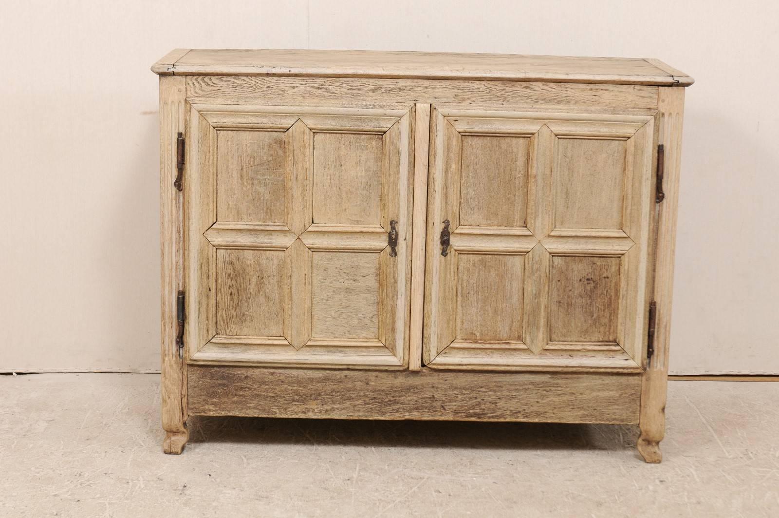 A French 18th century wood cabinet. This French buffet of bleached oak features two doors, each with four recessed panels, which open with a key to an inner shelf. There are squared, inset panels at each chest side, fluted side posts, and clean