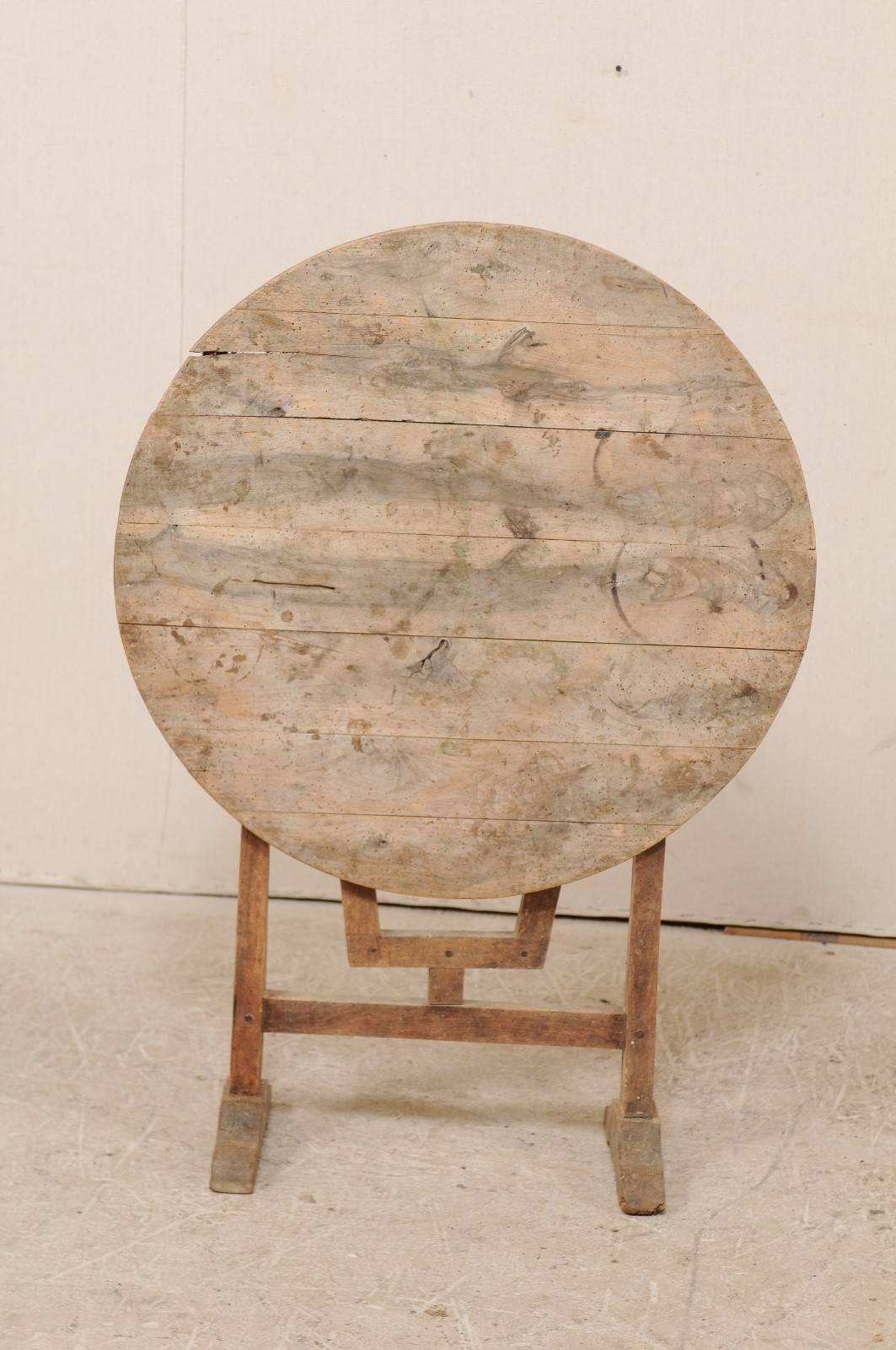 A French 20th century wine tasting table. This round shaped French wine tasting table has a natural wood finish with the typical tilt top, and butterfly wedge support. This smaller sized French wine tasting table would work well in a wine cellar or