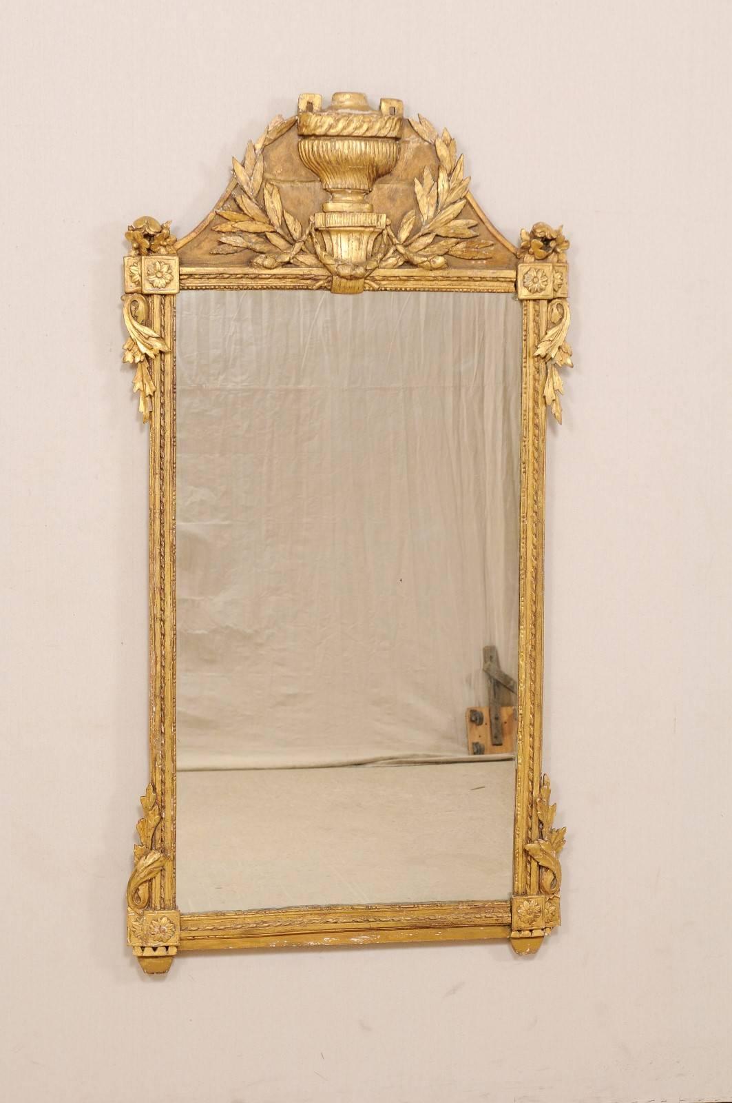 A French 18th century richly carved and gilded wood mirror. This French tall giltwood rectangular wall mirror features a wonderfully carved crest with leaves and urn at it's centre. There are sweet floral and leafy accents at each the mirror's