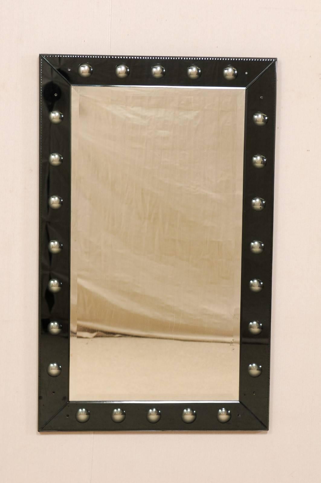 A vintage American mirror with bullseye surround. This American rectangular shaped mirror is adorn with a series of small convex bullseyes throughout its border. The mirrored bullseyes are recessed beneath a tinted black glass surround, so that the