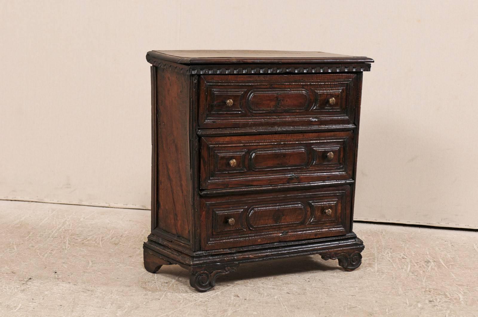 An early 18th century Italian three-drawer small commode. This antique Italian commode of dark walnut features three carved front doors, and an egg-and-dart molding motif along the top edge. This chest is raised upon bracket feet, the fronts which