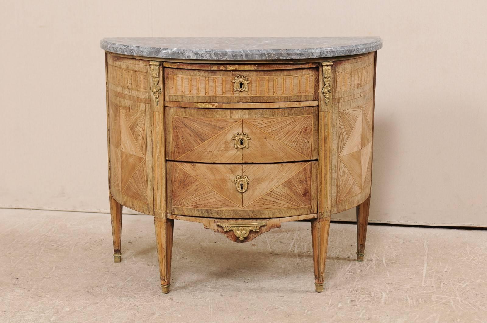 A French 19th century, demilune chest with honed marble top. This antique French three-drawer chest features beautiful marquetry details throughout the natural wood body with a honed marble top. The marquetry details lend themselves to a series of
