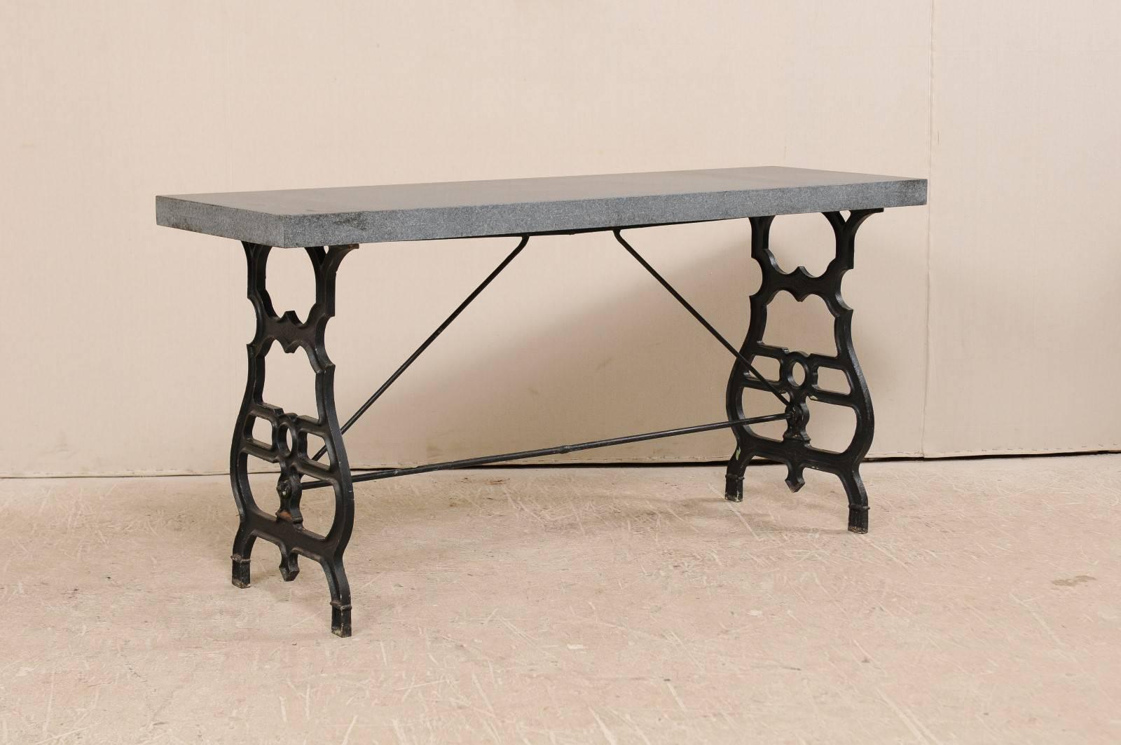 An antique French iron table with granite top. This French table, from the early 20th century, features a black iron base with a newer addition of a gray colored honed granite top. The base consists to two thin profiled sides, ornately forged and