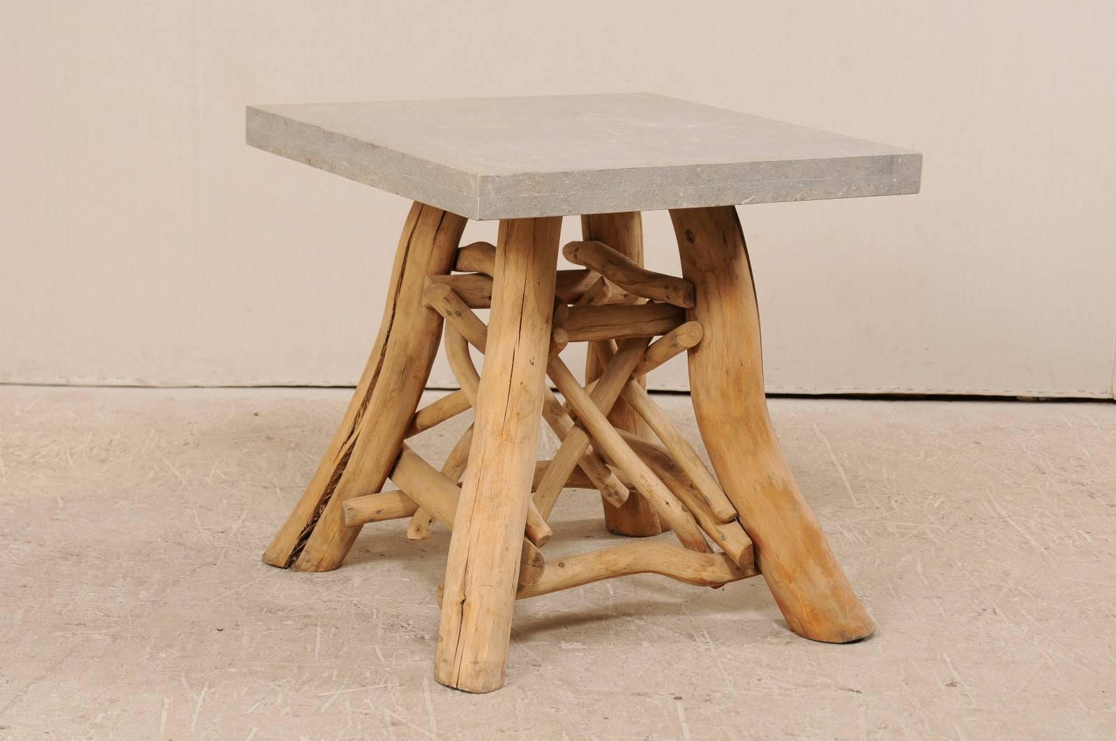 A vintage European occasional table. This wonderfully informal European occasional table features a thickly cut honed and fossilized stone top, square in shape, which is supported by four smoothed, natural wood limbs. The four larger limb feet have