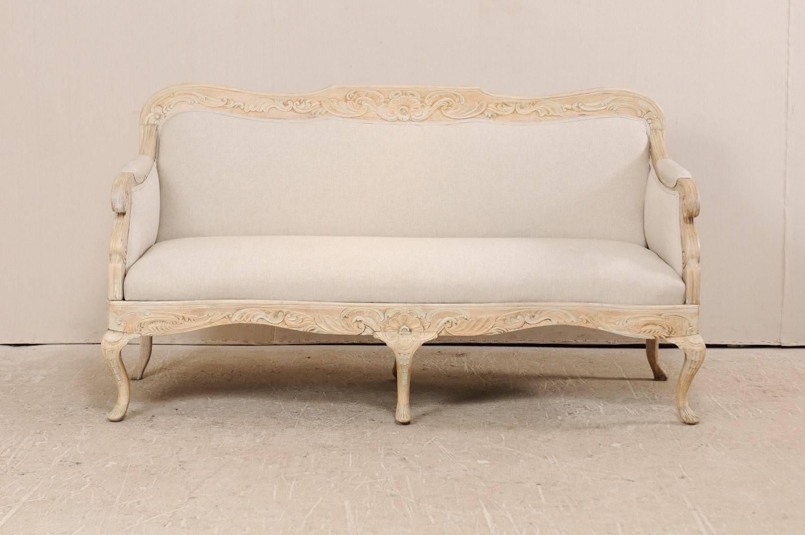 A Danish period Rococo sofa from the 18th century. This antique Danish sofa features a beautifully carved wood frame in a floral and leaf motif, carved scrolling knuckles, a gently valanced skirt, and cabriole legs. This sofa has been newly
