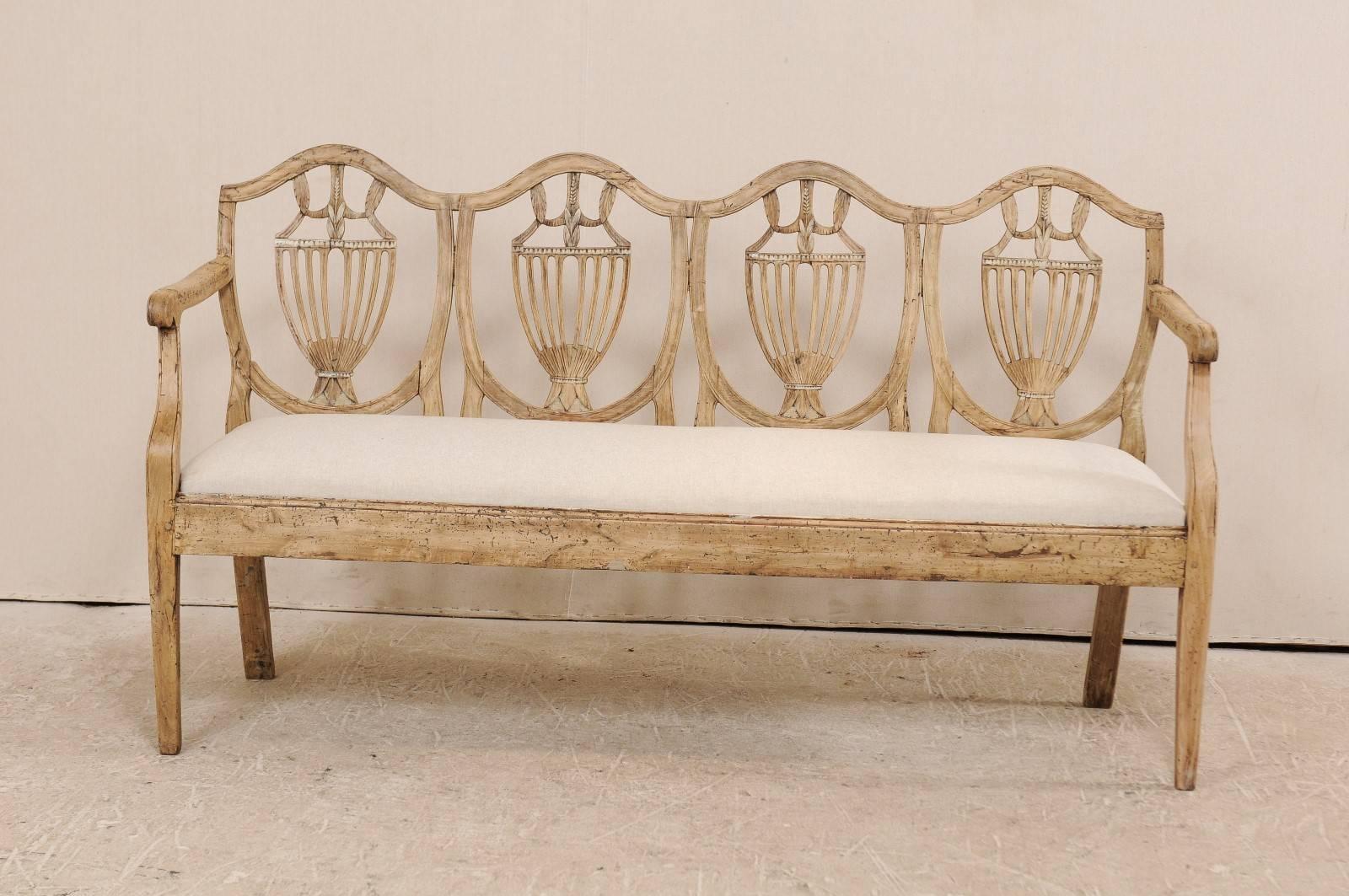 An 18th century Italian carved wood sofa bench. This antique Italian four-seat settee features a exquisitely carved pierced splat backs with a fluid top rail that rises and falls, giving definition to each seat. The sofa has a plain skirt, carved