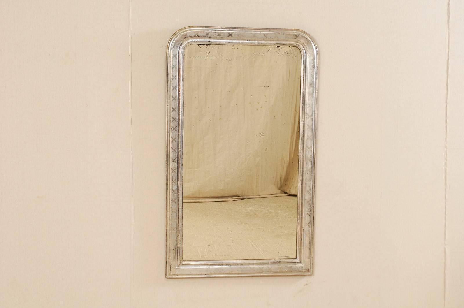 An antique French silver gilt Louis-Philippe style mirror. This French Louis-Philippe style mirror from the late 19th-early 20th century features a silver gilt carved wood frame with faint X-shaped patterns repeating about the surround. This mirror