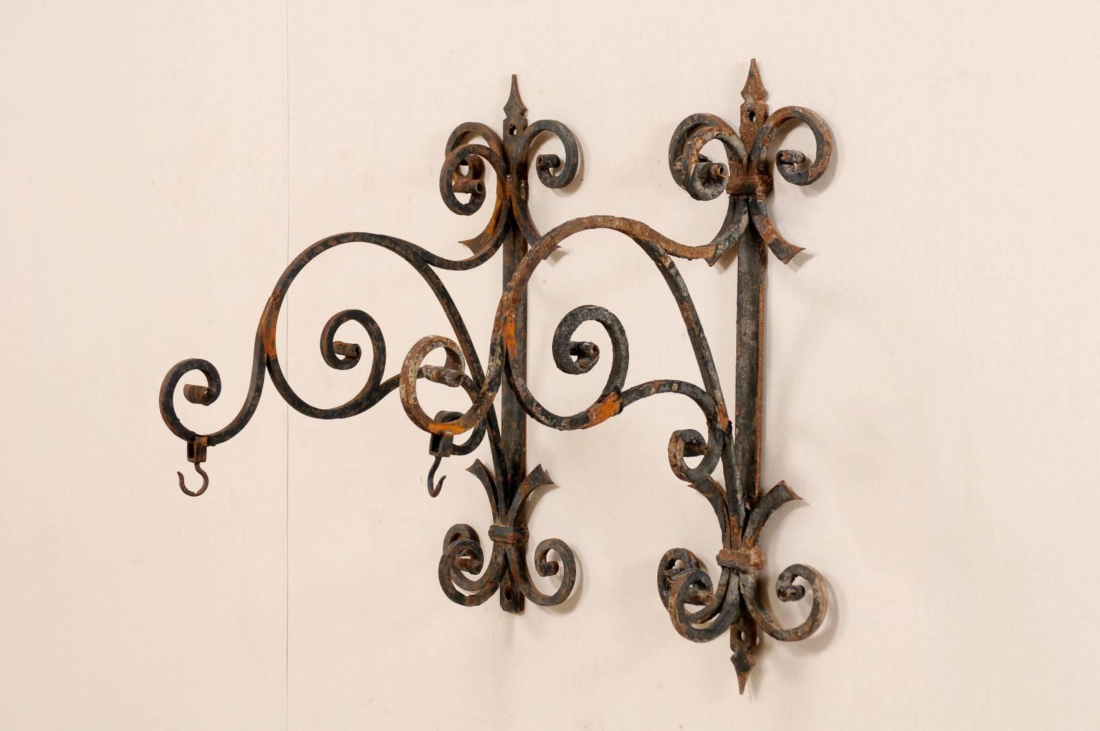 A pair of Italian, 19th century iron hangers. This pair of large-sized antique hangers from Italy feature a vertical back plate which supports the scrolling arms that extend out more than 2 feet. The upper and lower portions of the backplate