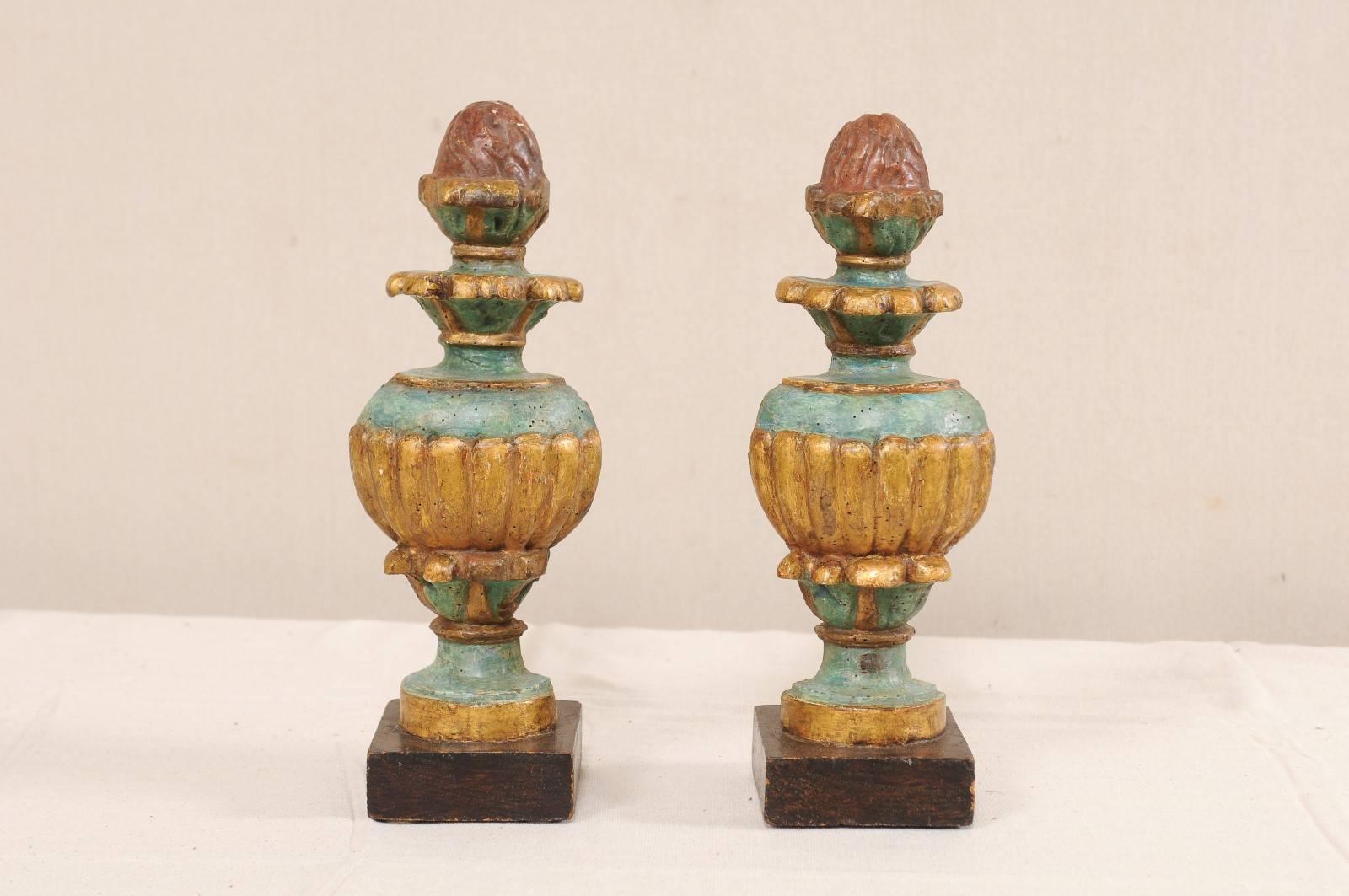 A pair of Italian 18th century carved and painted wood fragments. These elegant antique Italian carved wood urn fragments have a lightly marbleized blue/green finish with red and gold accents. The urns are raised on brown, square-shaped bases. Note