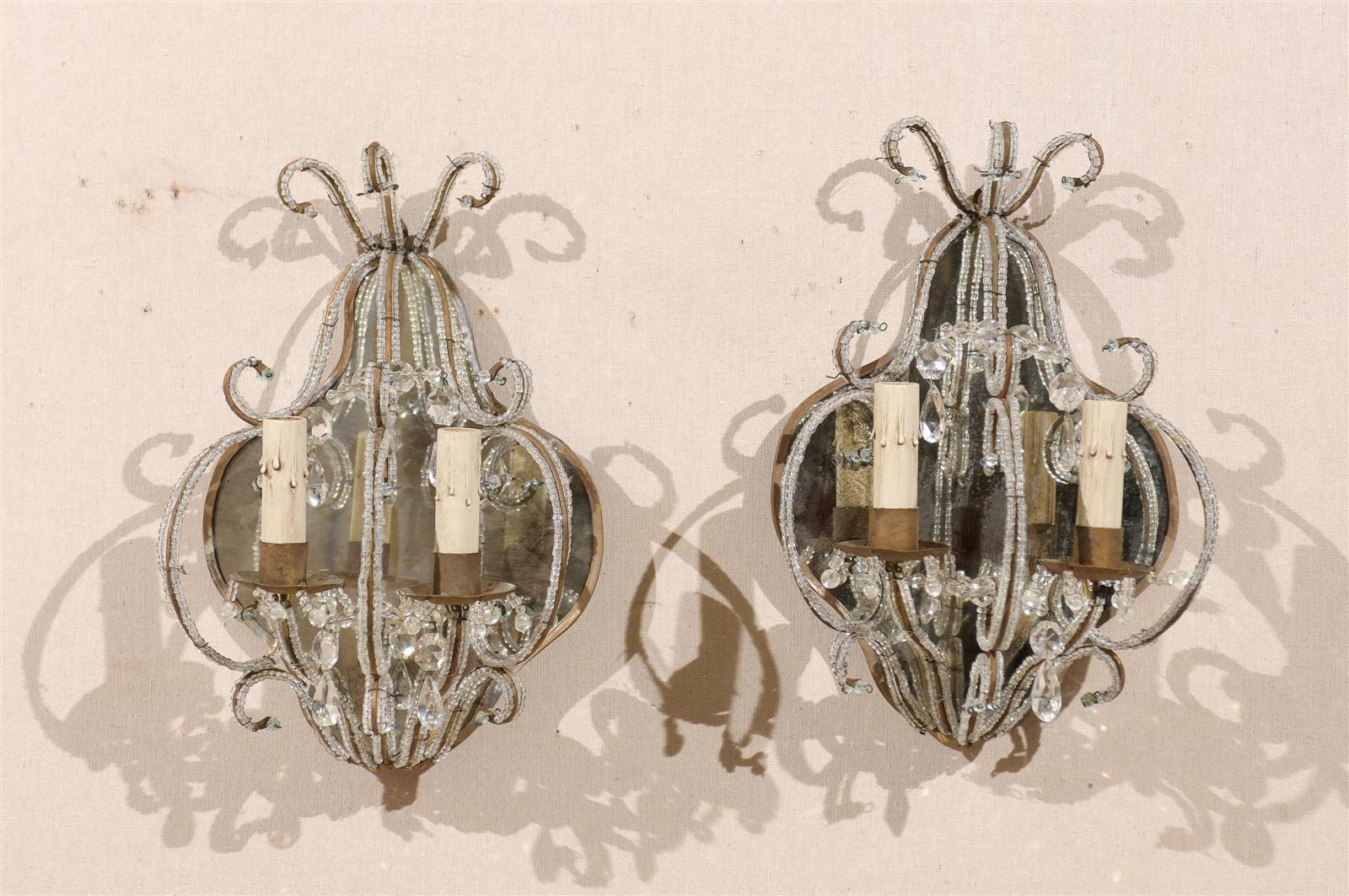A pair of Italian 20th century two-light mirror-back crystal sconces. This pair of Italian sconces features gilded armature and beaded decor. The flowing c-scrolls give this pair an elegant look. These sconces have been rewired for the United States.
