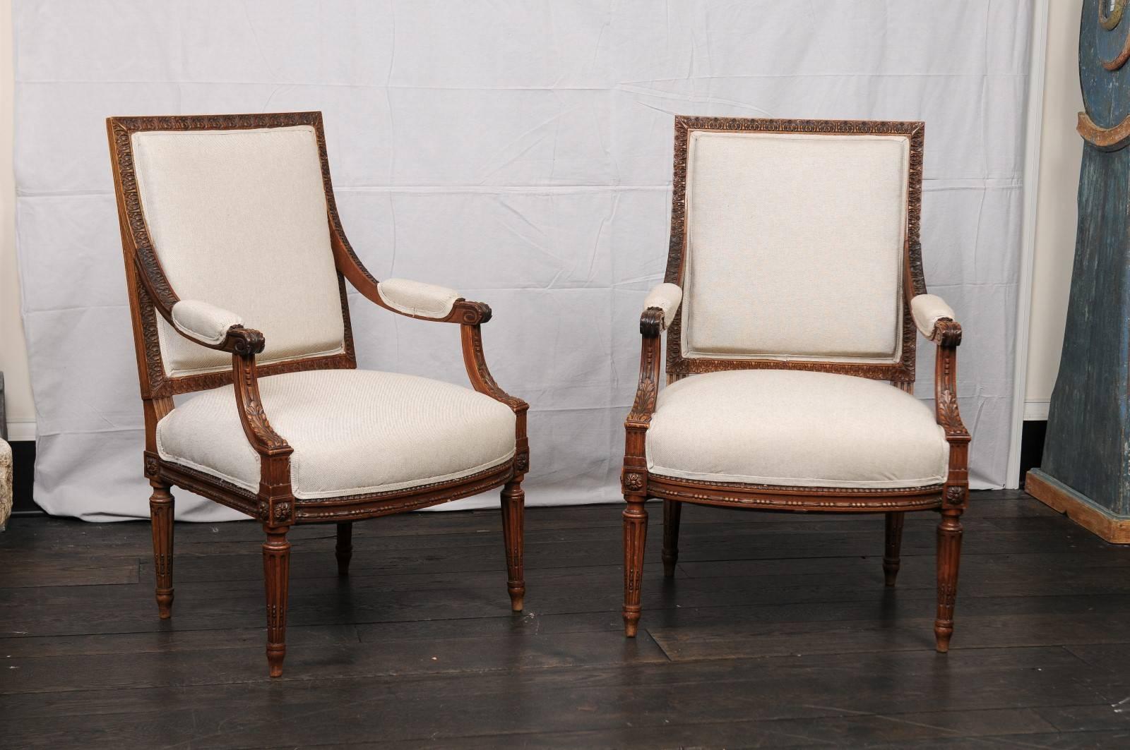 A pair of mid-20th century French Louis XVI style armchairs. This pair of French armchairs have beautiful, tightly carved details throughout which feature a repeating pattern of single flower and leaves about the chair back frame, scrolled knuckles