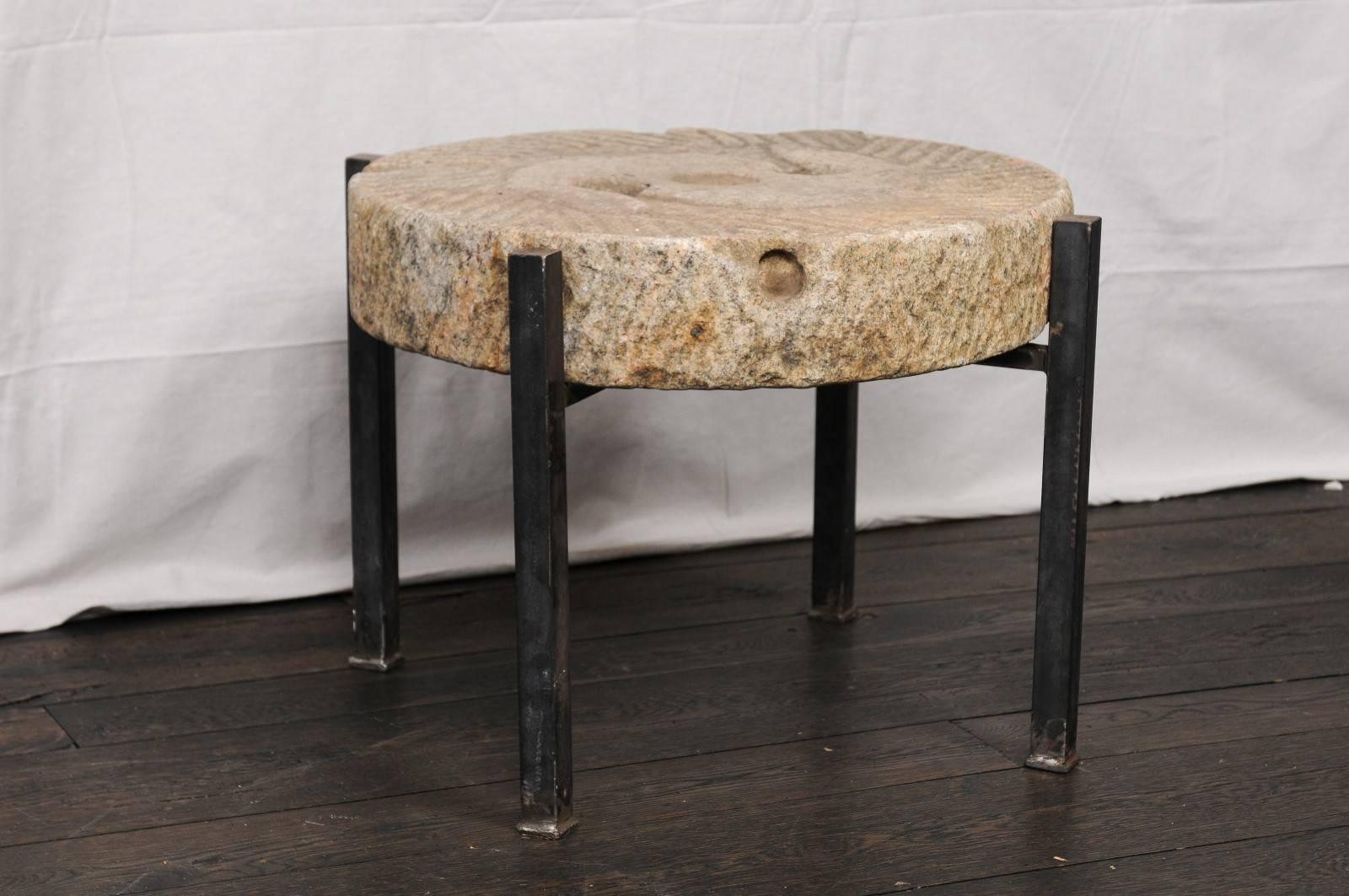 A 19th century European millstone grinding table. This fantastic little drinks table features an antique milling and grinding stone which rests upon a new, custom, black iron base. This stone has lovely texture and ridges, and was originally used in