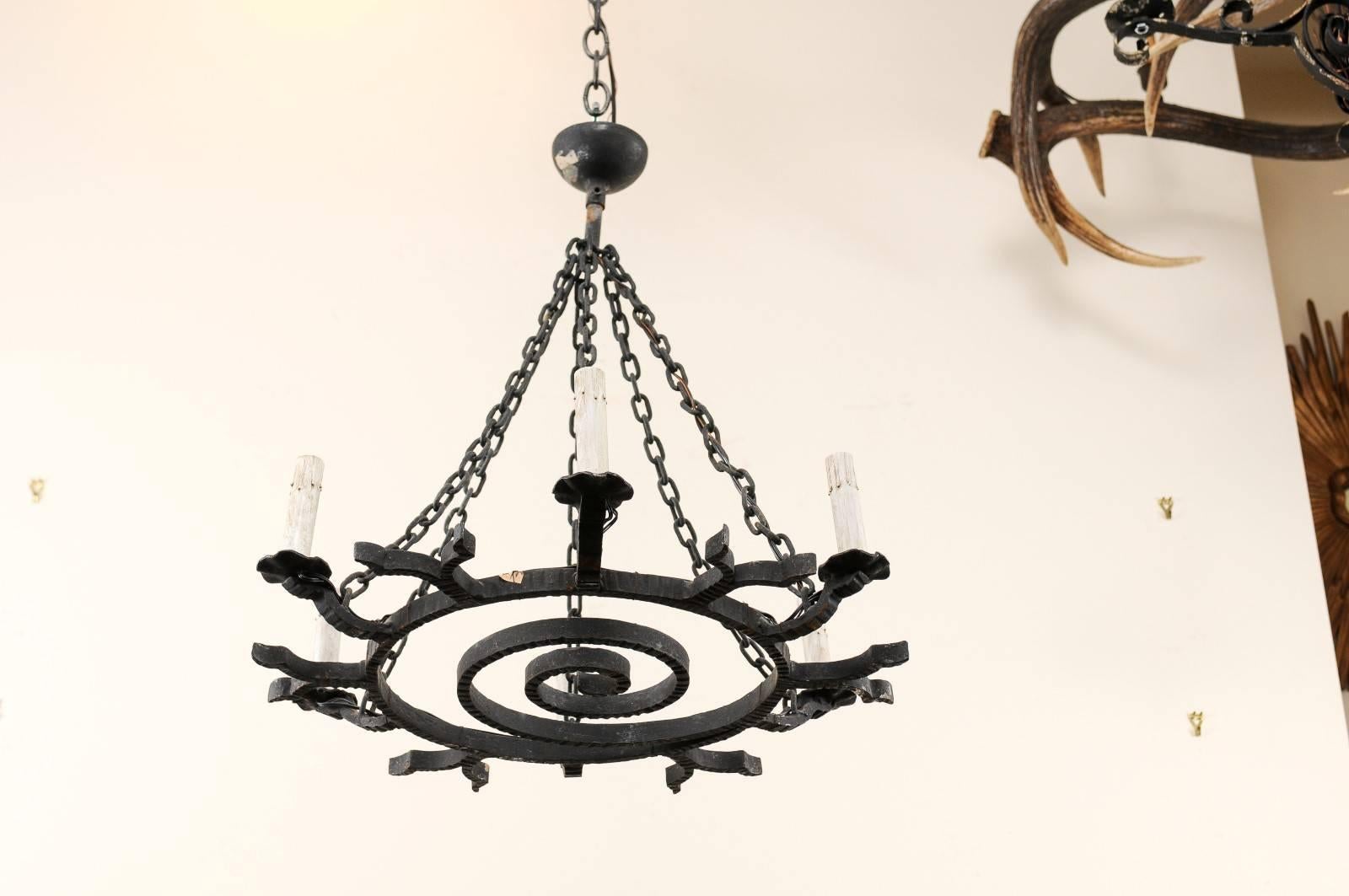 A French forged iron chandelier from the 1950s. This unique French mid-century chandelier has a whimsical spiral decoration filling up its central ring. There are six lights which lift up and away from the middle ring with alternating with