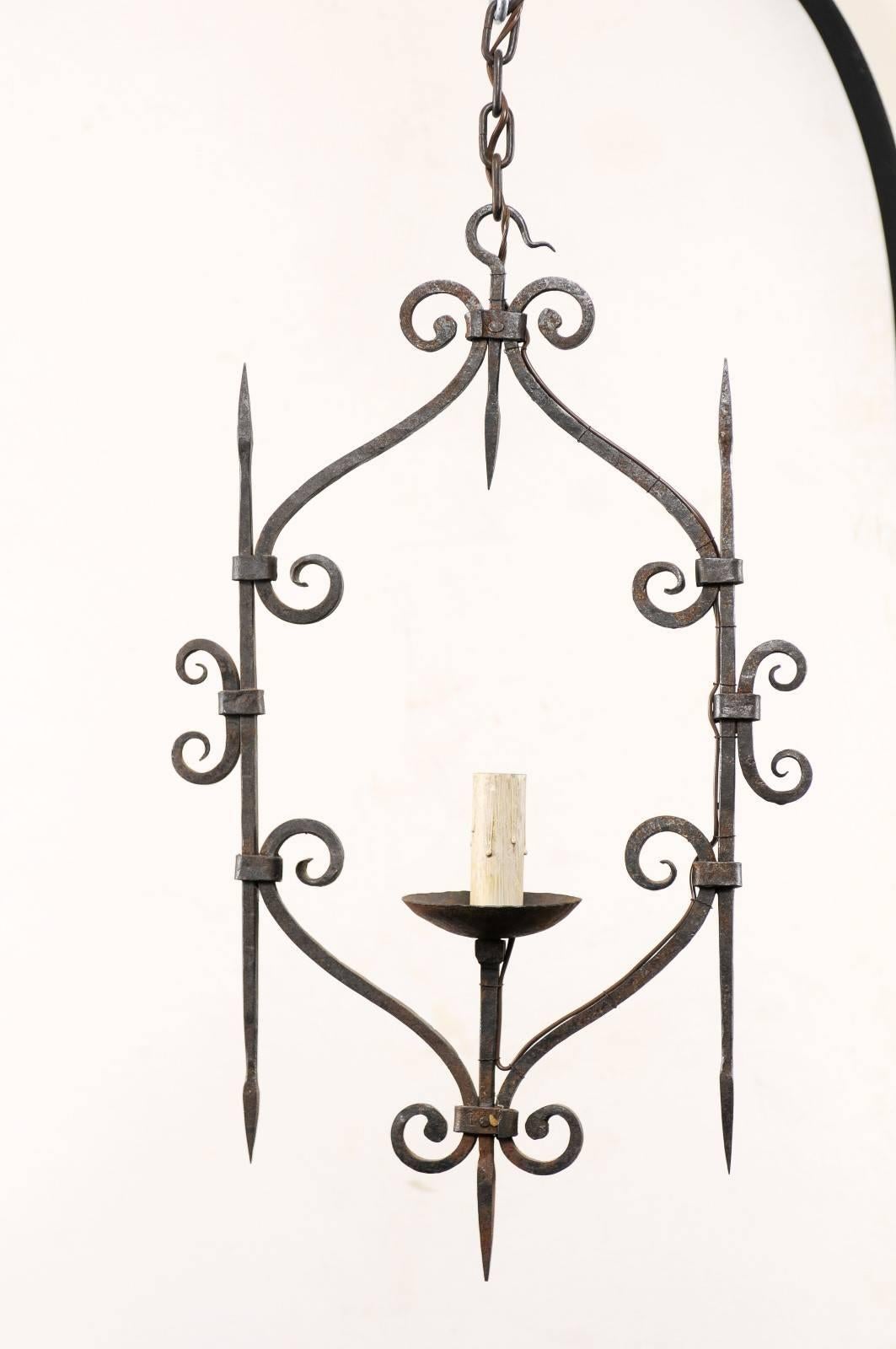 A French single light iron chandelier from the mid-20th century. This French vintage light fixture features a single light in its centre, framed sweetly between two lateral spires. The chandelier is decorated with hand-forged scroll details about