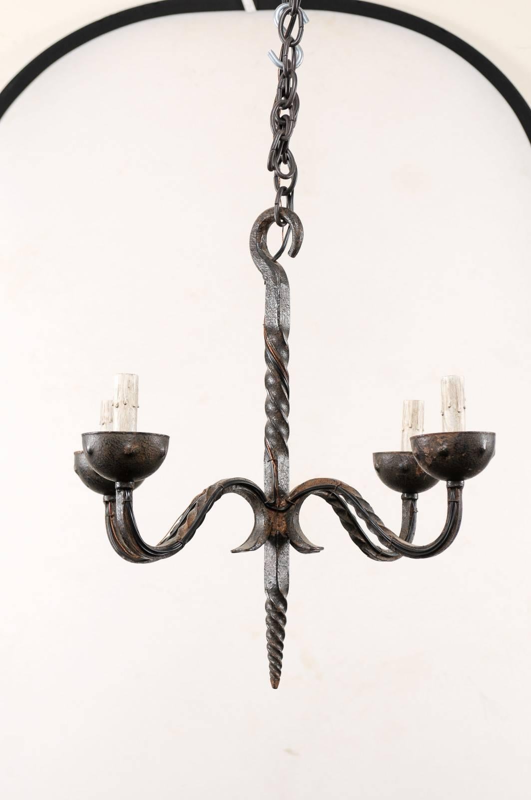 A French vintage four-light wrought iron chandelier. This mid-20th century French chandelier features a central metal twisted central column with four swagged and nicely twisted arms flowing out from it's centre. The arms each terminate into cupped
