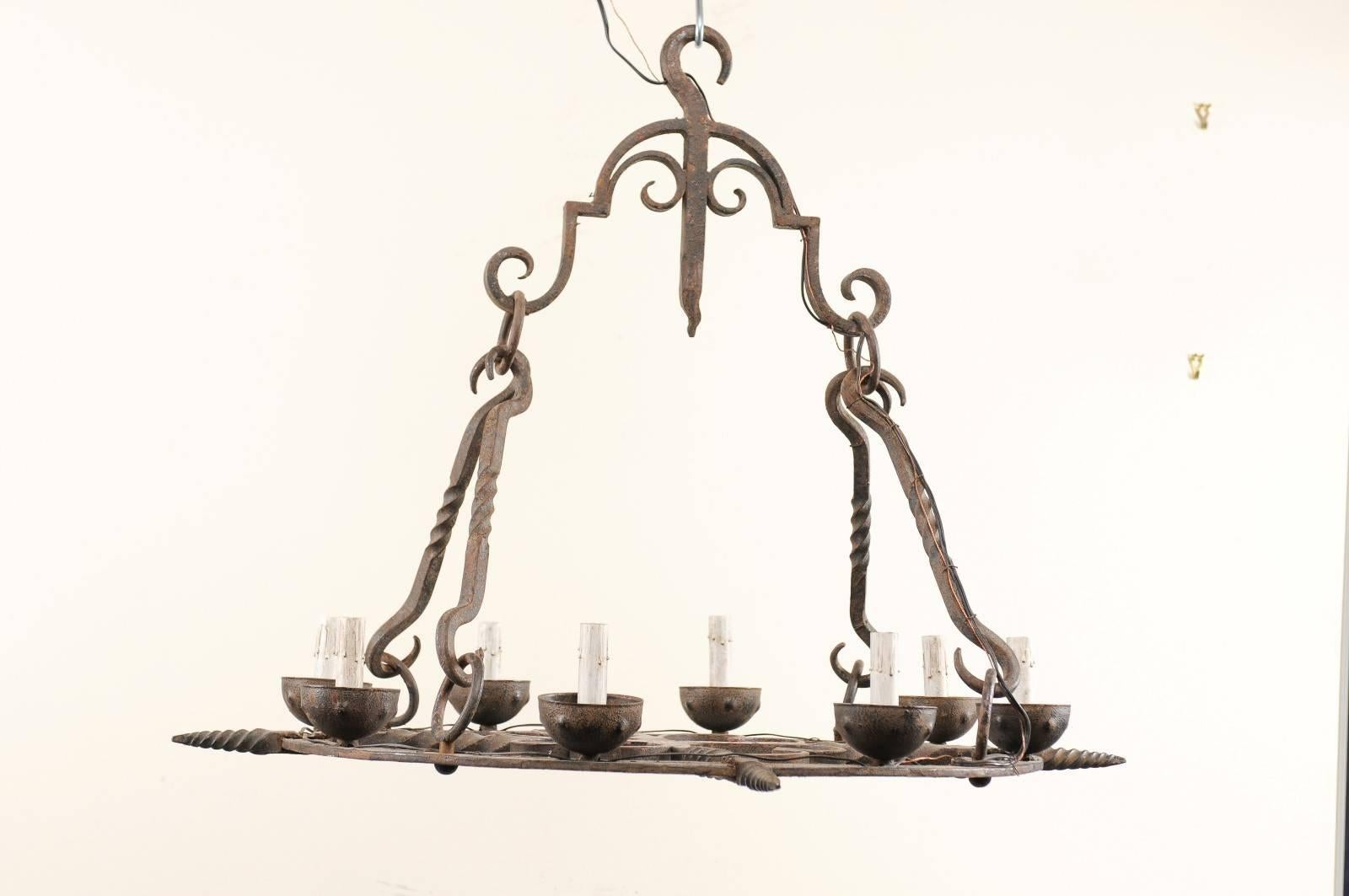 A French mid-century eight-light hand-forged iron chandelier. This mid-20th century chandelier from France, of artfully crafted forged iron has a flattened, circular shaped body which supports the eight iron bobèches and candle covers around it's