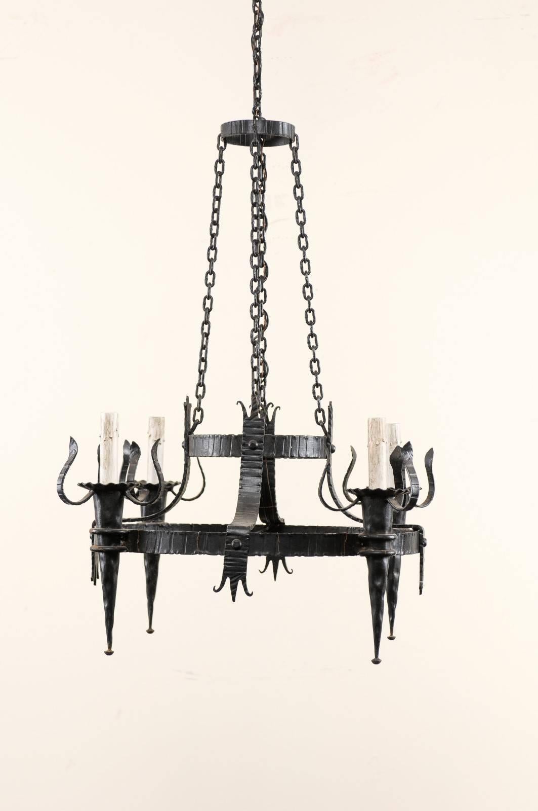 A French vintage four-light black iron chandelier. This French iron chandelier from the mid-20th century features a larger ring with four torch style lights around it's perimeter, connected by decorated iron strips to a smaller second tier at it's