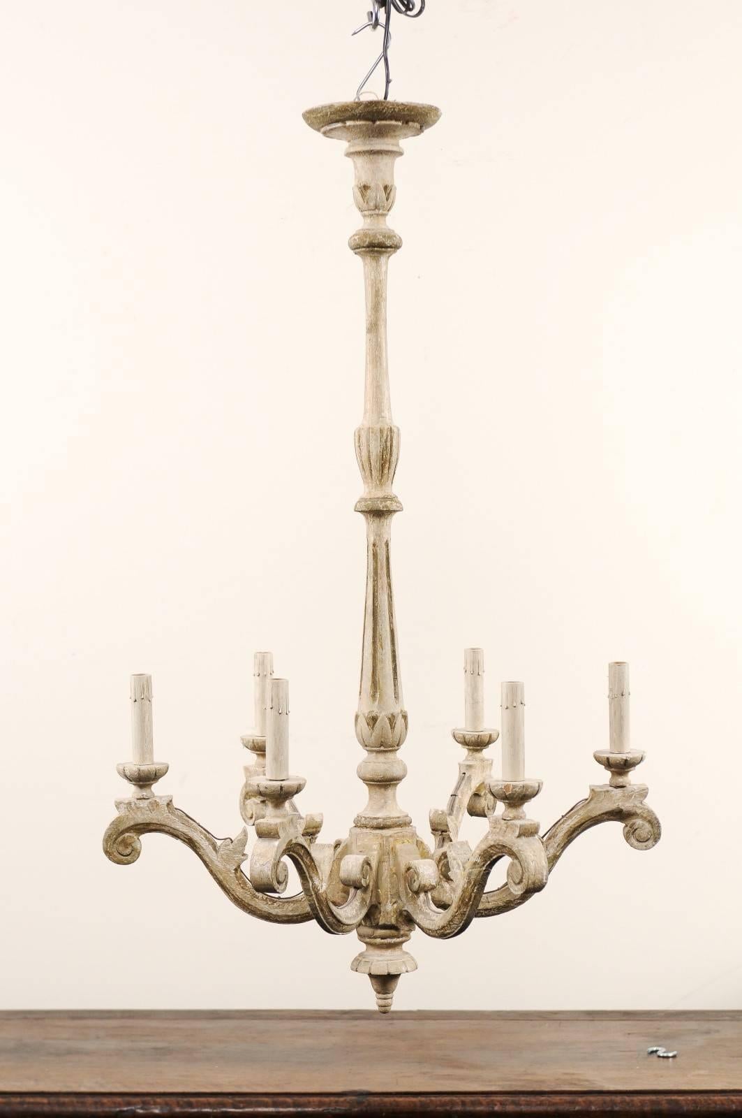 An elegant pair of French carved and painted wood six-light chandeliers from the mid-20th century. This pair of French chandeliers each feature long, slender carved central columns which lead down to six elegantly scrolled arms that lift up and