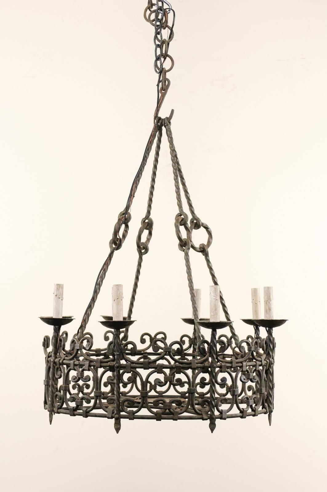 A French eight-light iron chandelier from the mid-20th century. This French midcentury chandelier features a central iron ring which is ornately decorated with a collection of c-scroll patterns throughout. There are eight torch-like lights set about