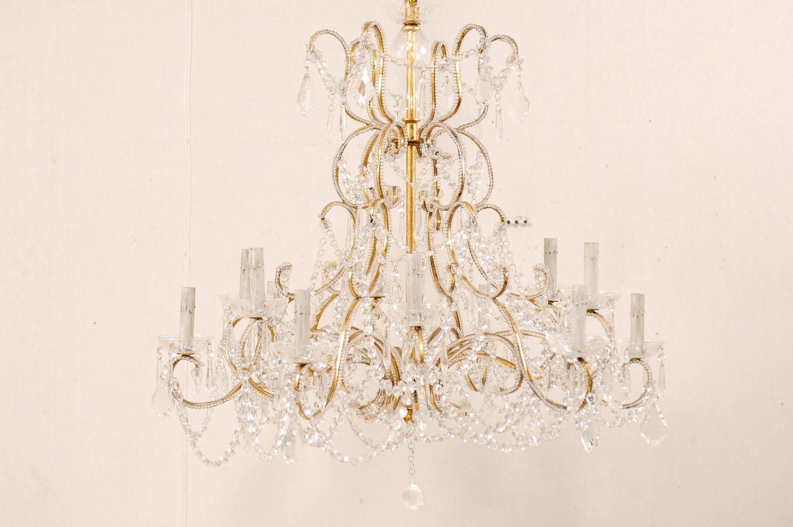 A French mid-20th century twelve-light crystal chandelier. This elaborate French crystal chandelier has twelve lights distributed in an undulating fashion about its center post, supported by scrolling arms, draped in crystals. The gilded iron